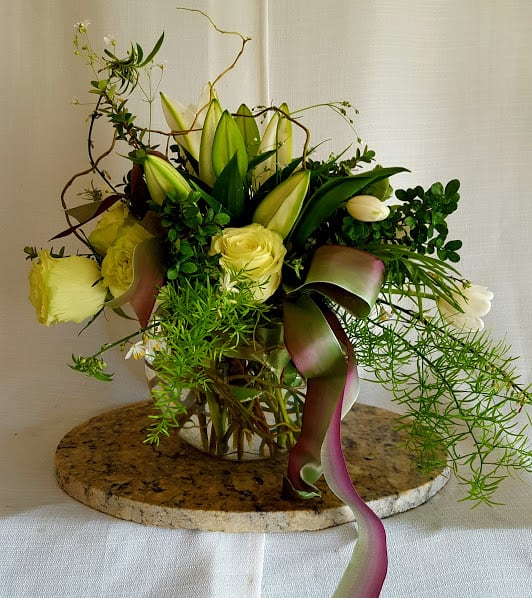 Yellow roses and lilies in a glass vase with trailing ribbon