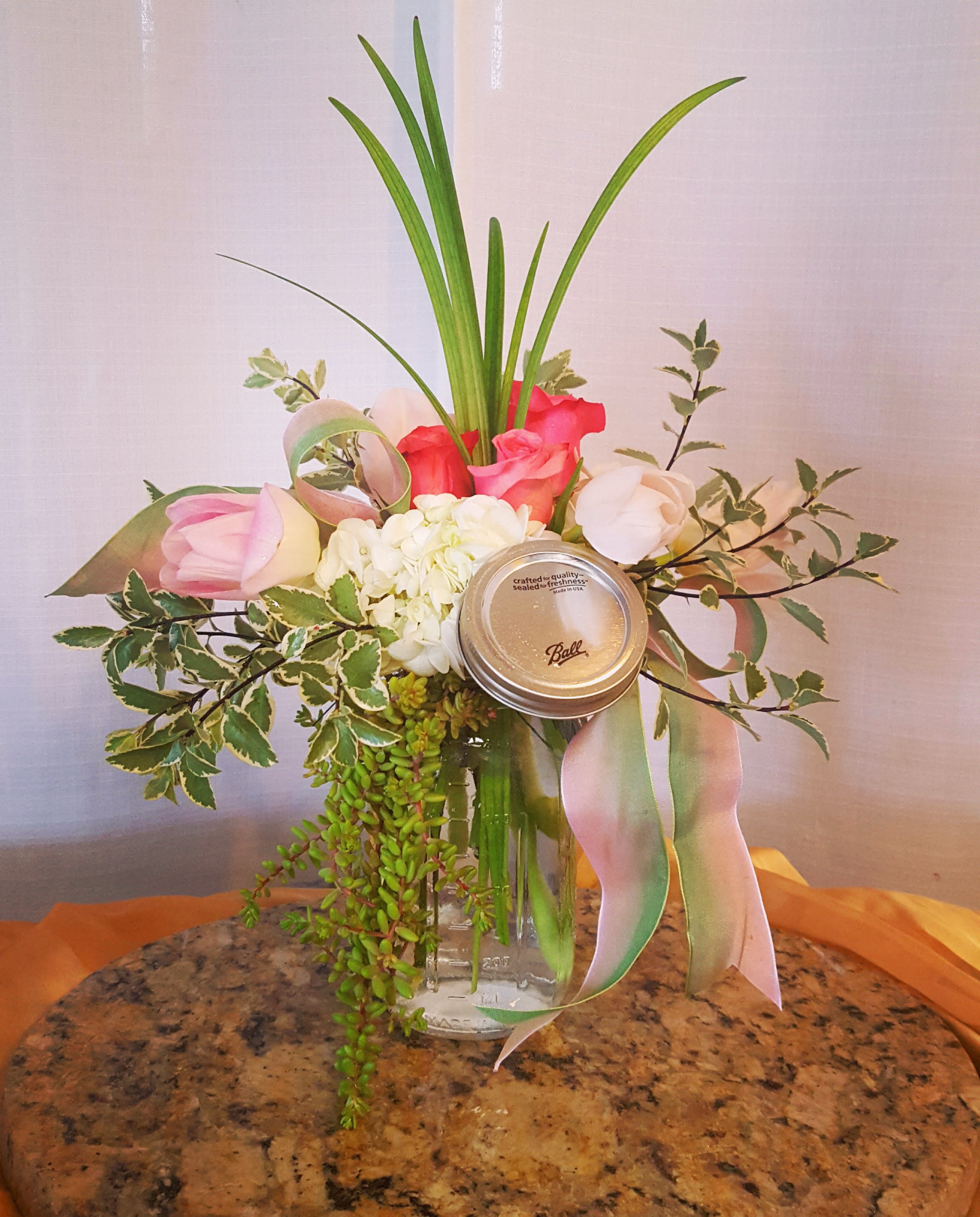 Pink and white floral arrangement in a glass jar with a ribbon and mason jar lid