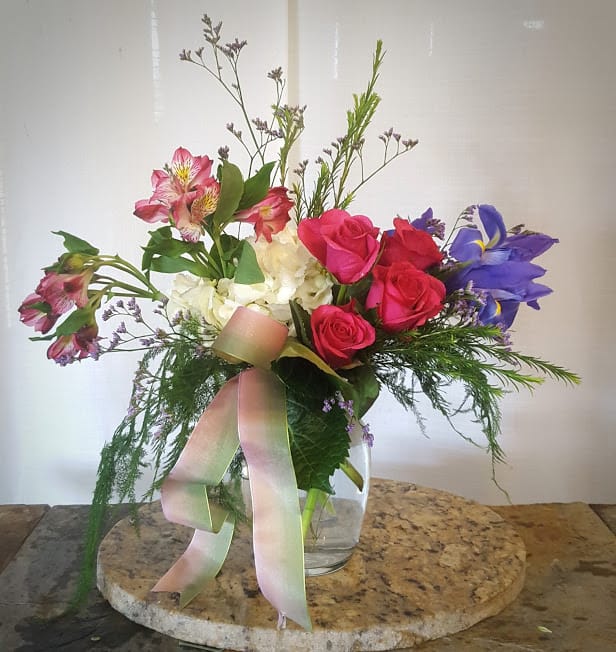 Mixed bouquet of roses, alstroemeria, and irises in a glass vase with ribbon