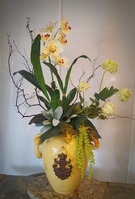 Tall floral arrangement with yellow orchids in a decorative ceramic vase
