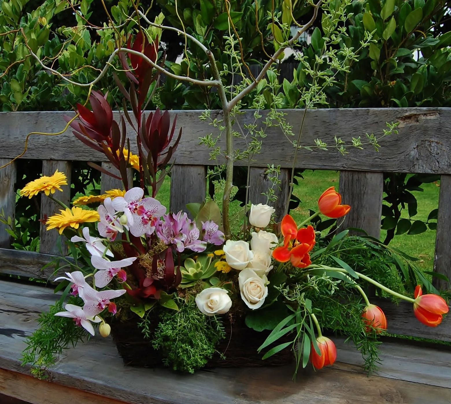 Mixed floral arrangement with orchids, roses, tulips, and yellow daisies