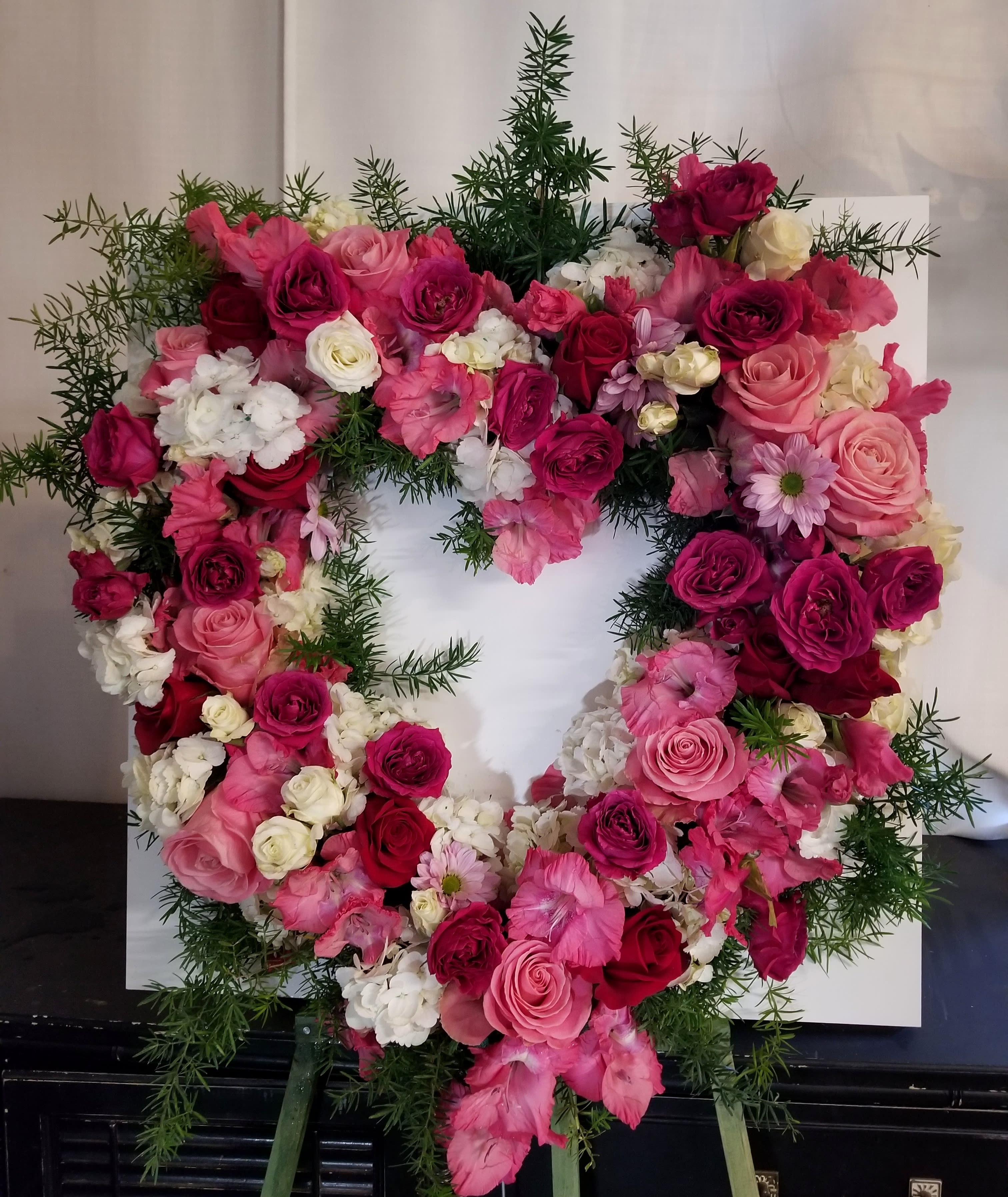 Heart-shaped floral wreath of pink and white roses with greenery