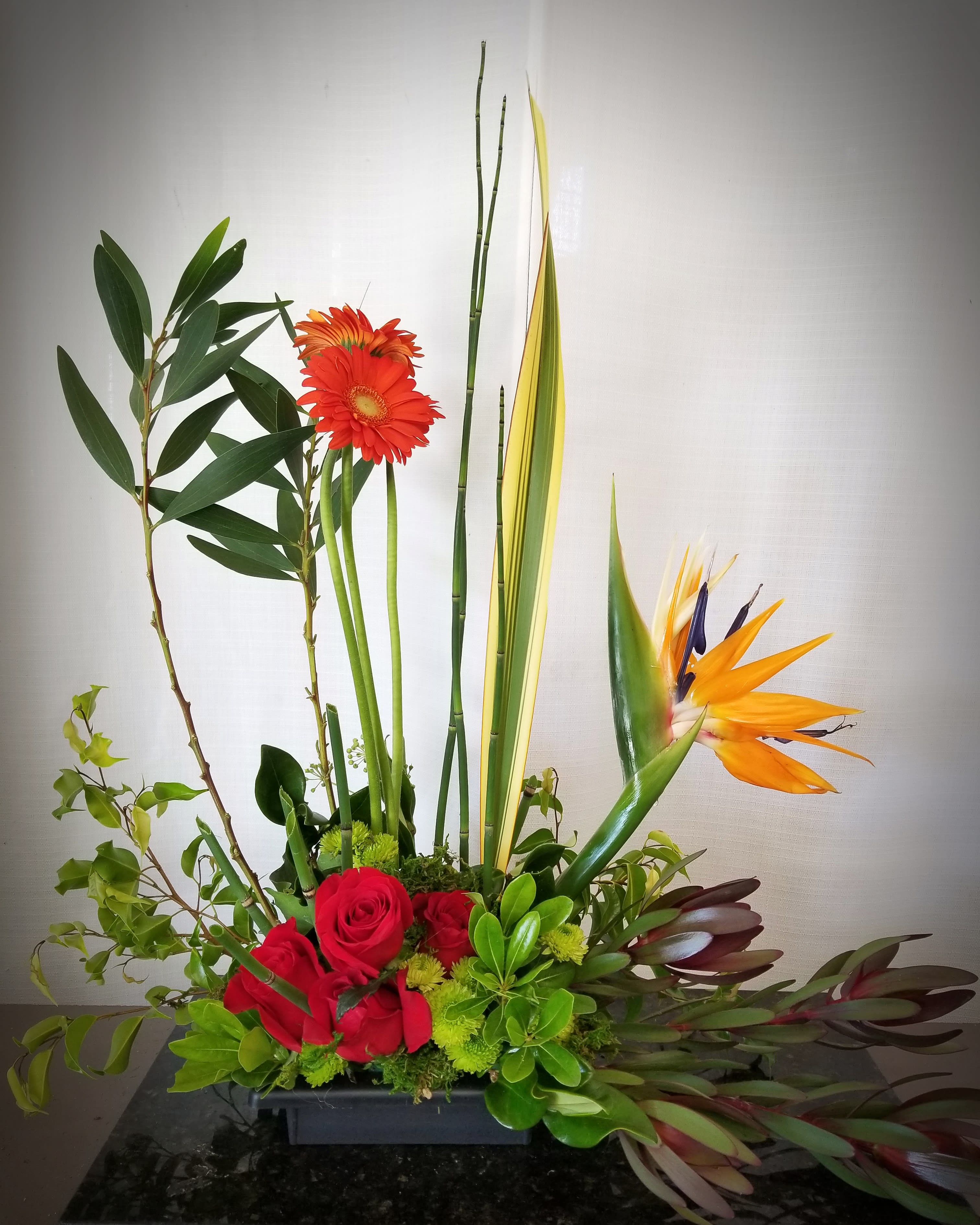 Tropical floral arrangement with red roses, orange gerberas, and bird of paradise