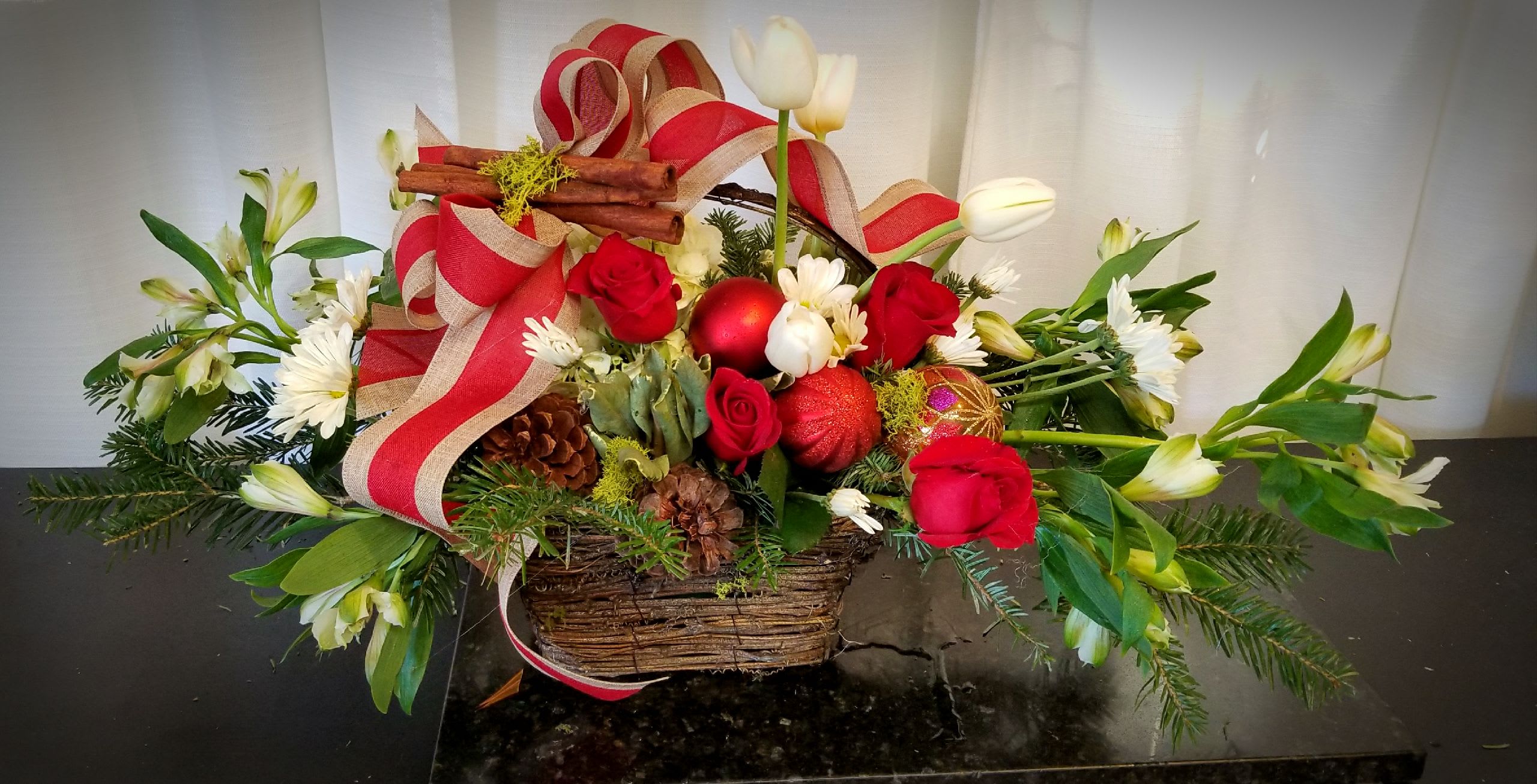 Basket arrangement with red roses, white flowers, and holiday ribbon