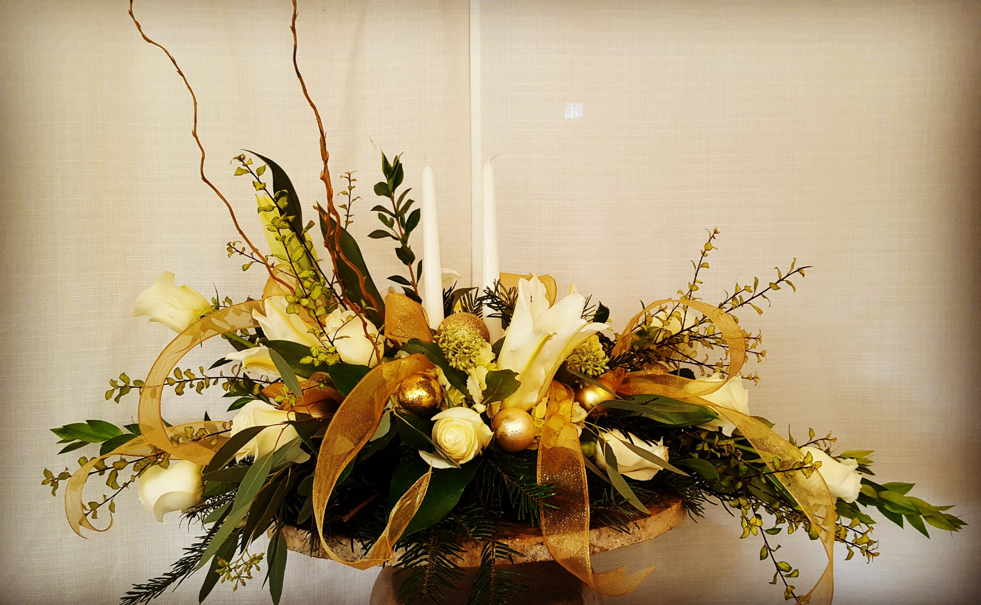 White floral centerpiece with gold ribbon and candles in a low container