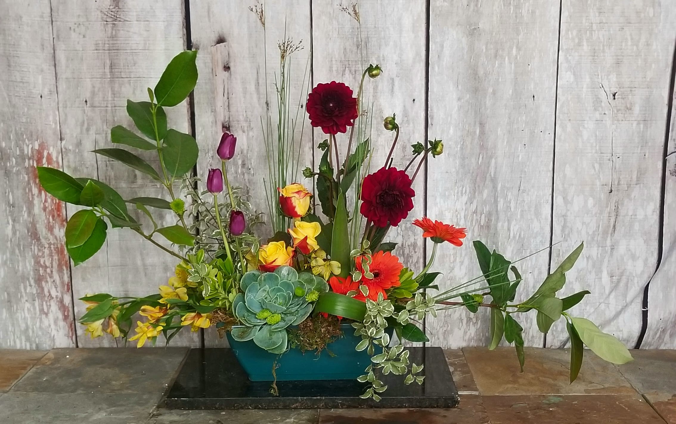 Mixed floral arrangement with red, orange, yellow, and purple blooms in a teal container