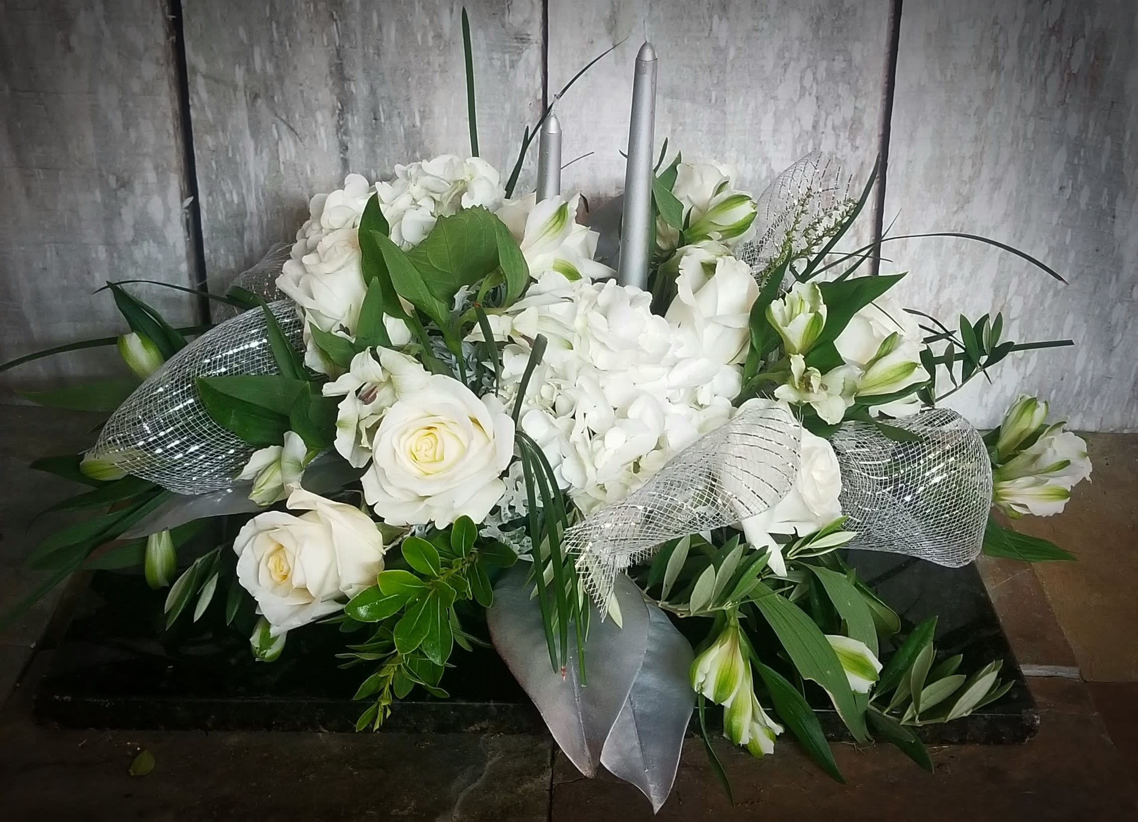 White floral arrangement with roses, hydrangeas, and lilies in a low container
