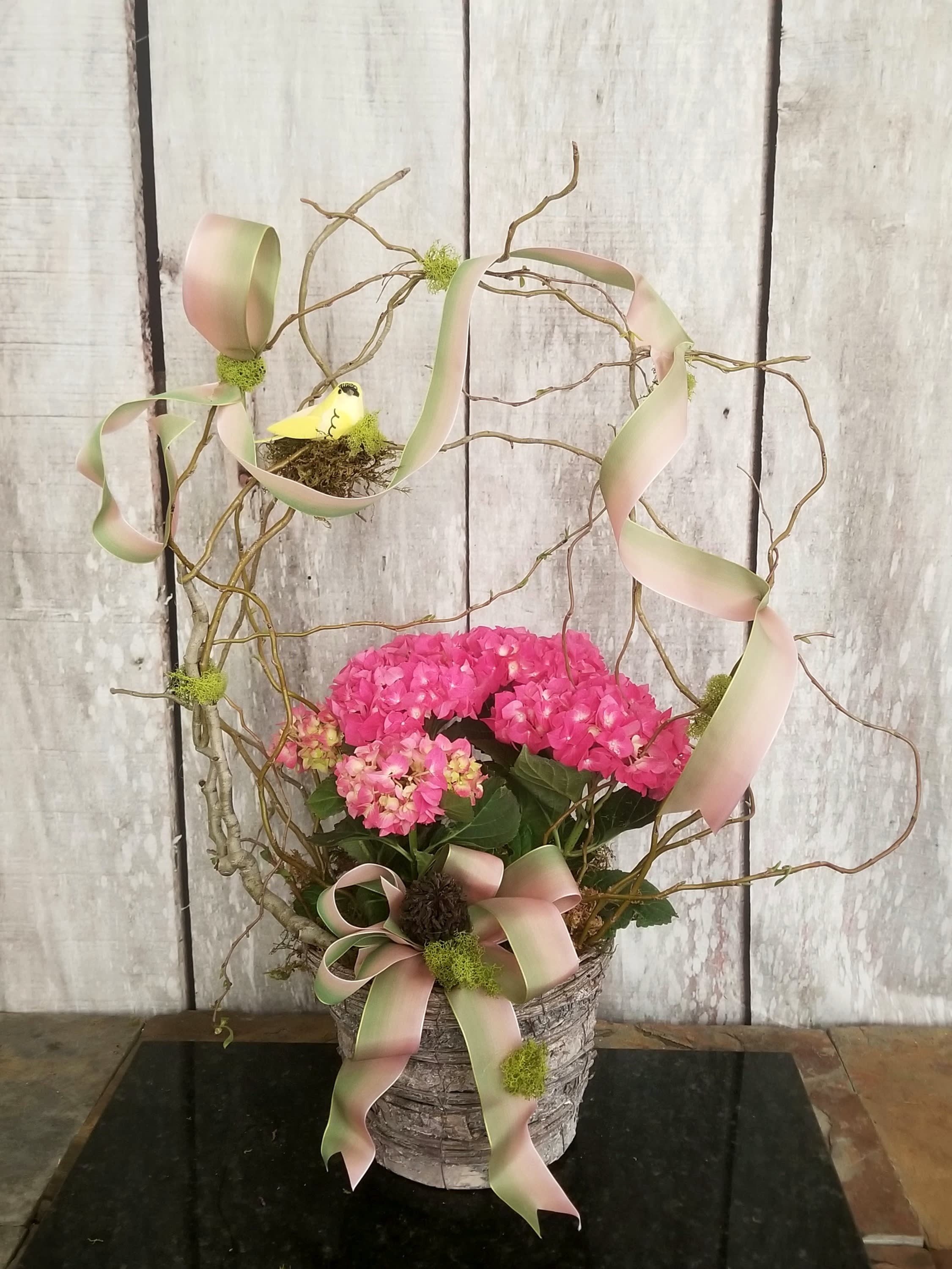 Pink hydrangea arrangement in a rustic basket with ribbon and twig accents