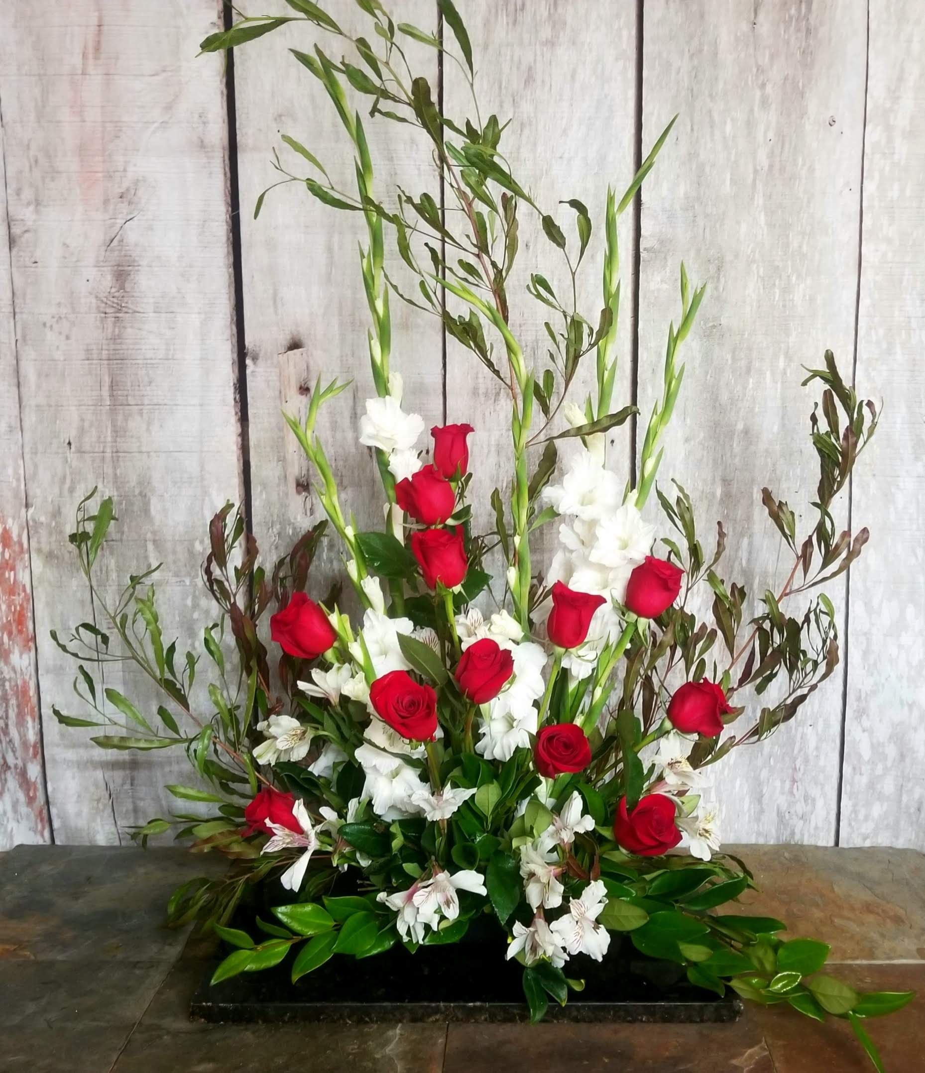 Tall floral arrangement with red roses and white flowers in a low black container
