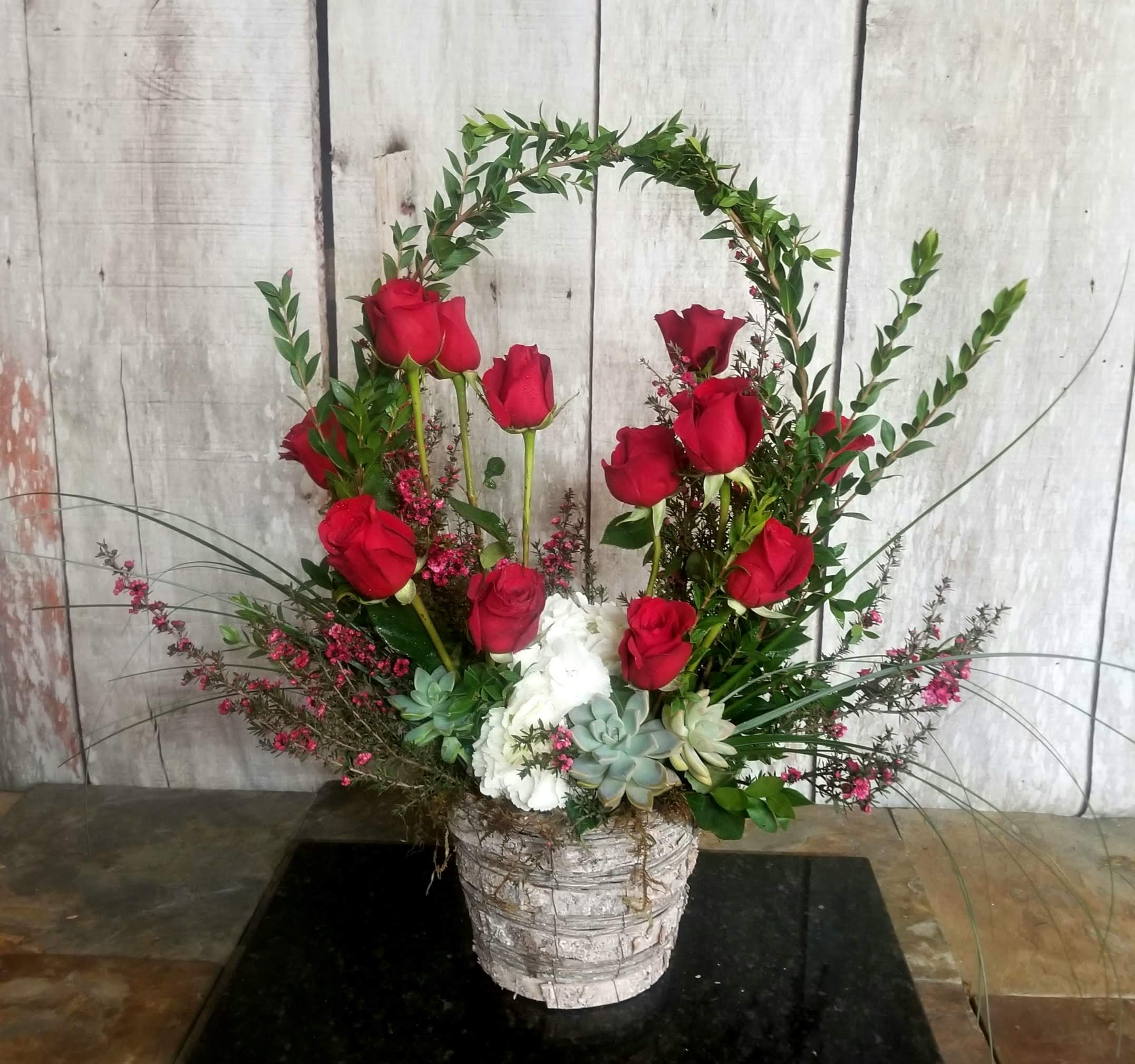Red roses arranged in a white basket with succulents and greenery