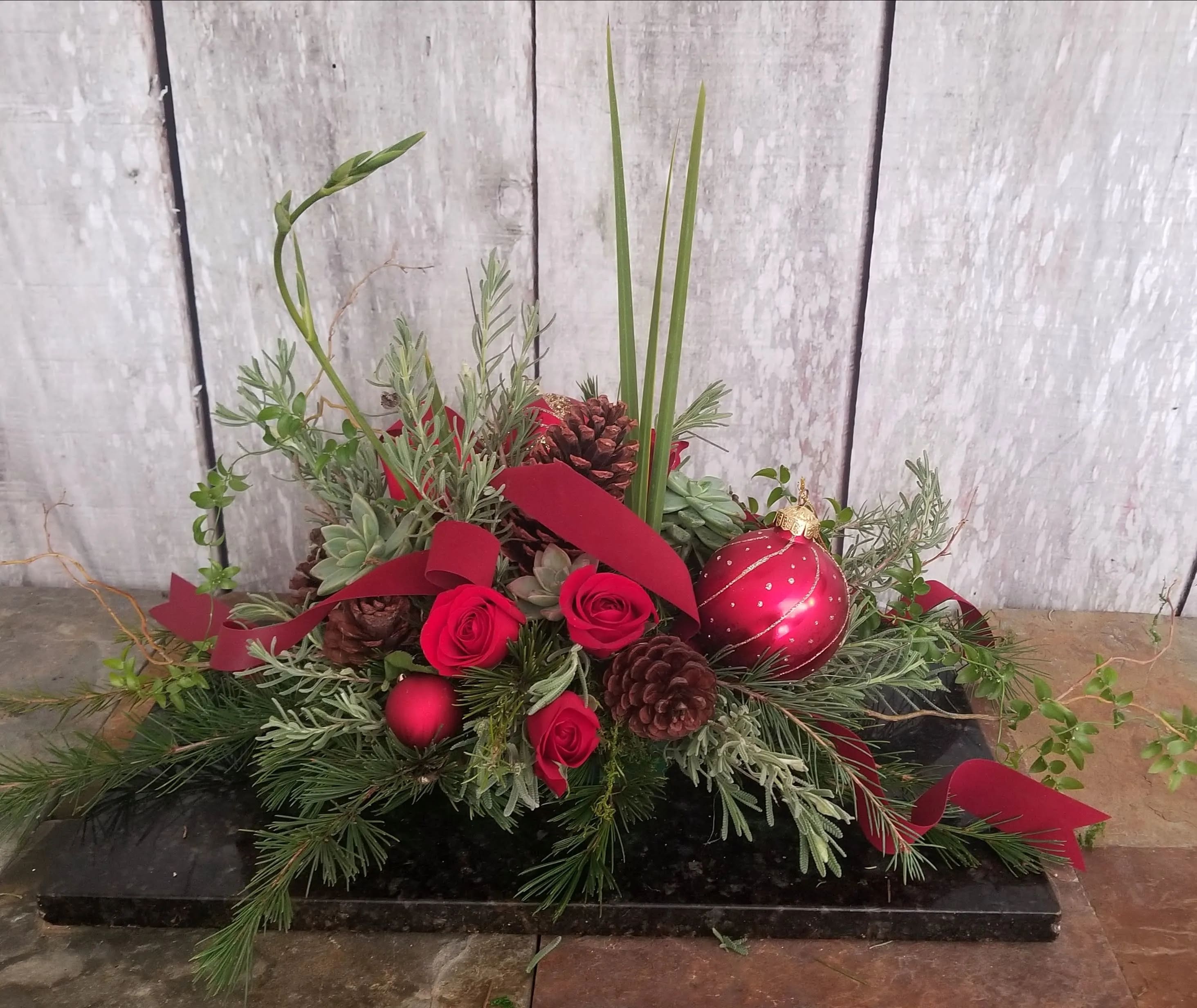 Red roses and pinecones arranged with holiday greenery and a red ornament