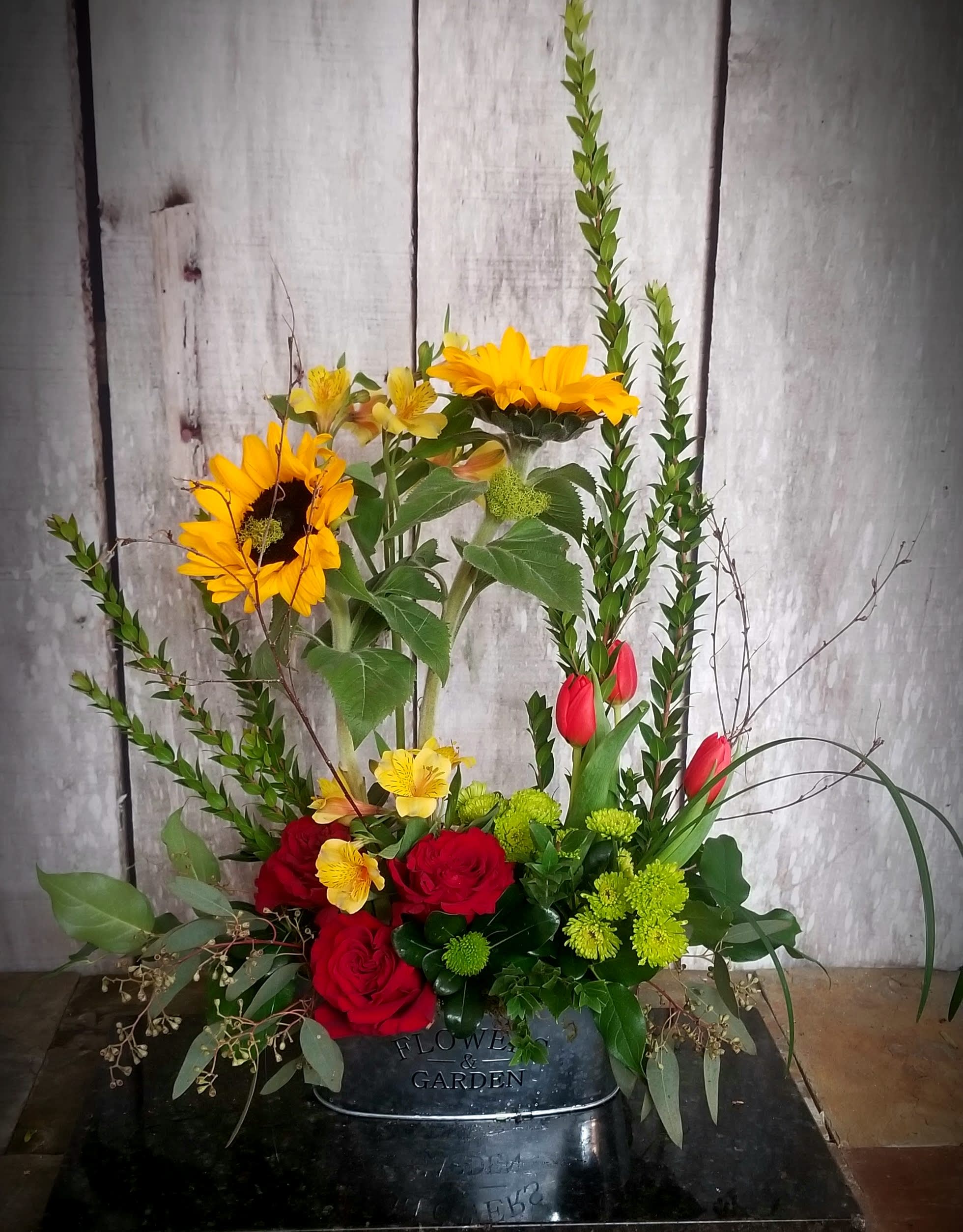 Mixed floral arrangement with sunflowers, red roses, and tulips in a black container