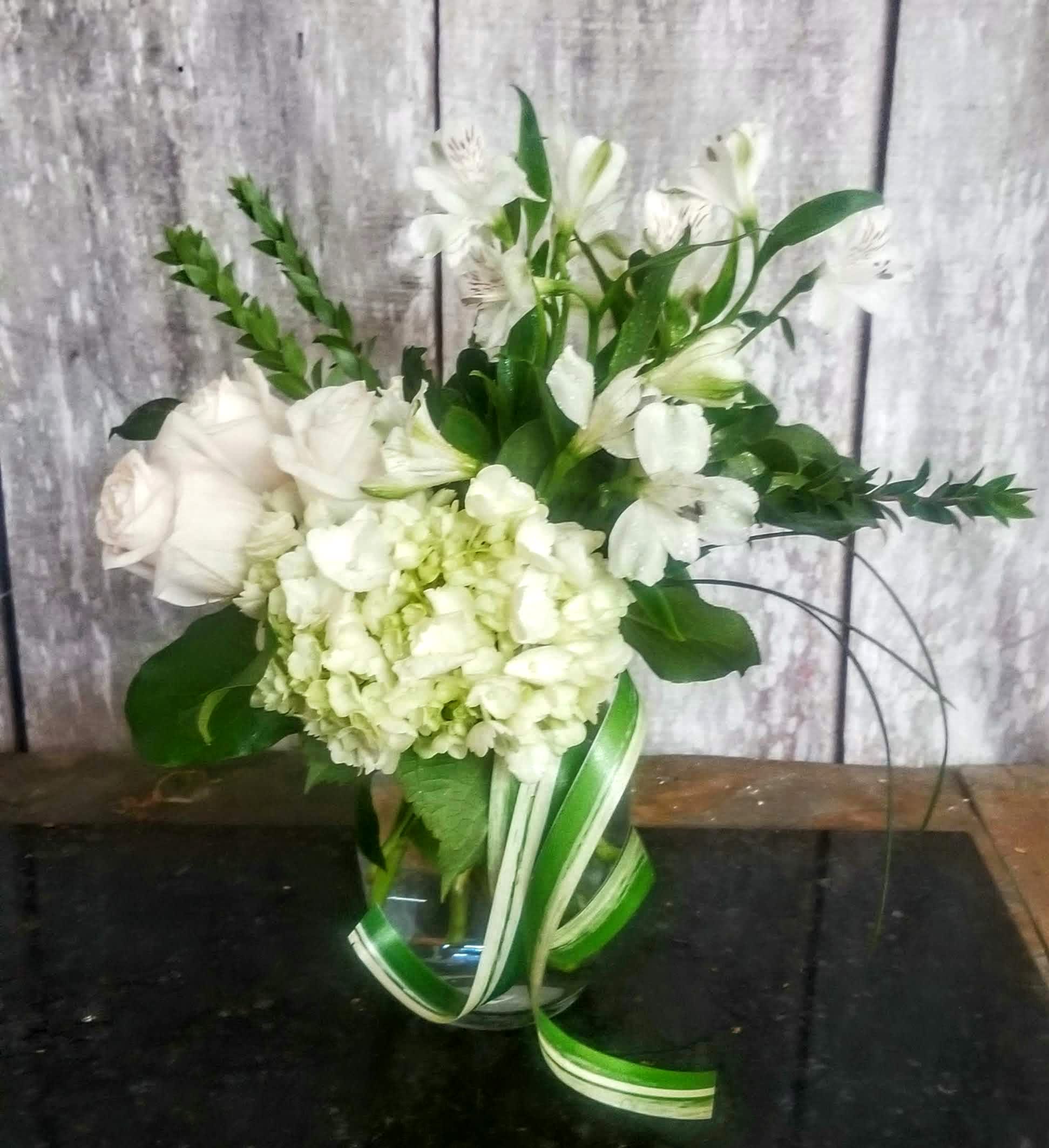 White floral arrangement in a glass vase with ribbon accents