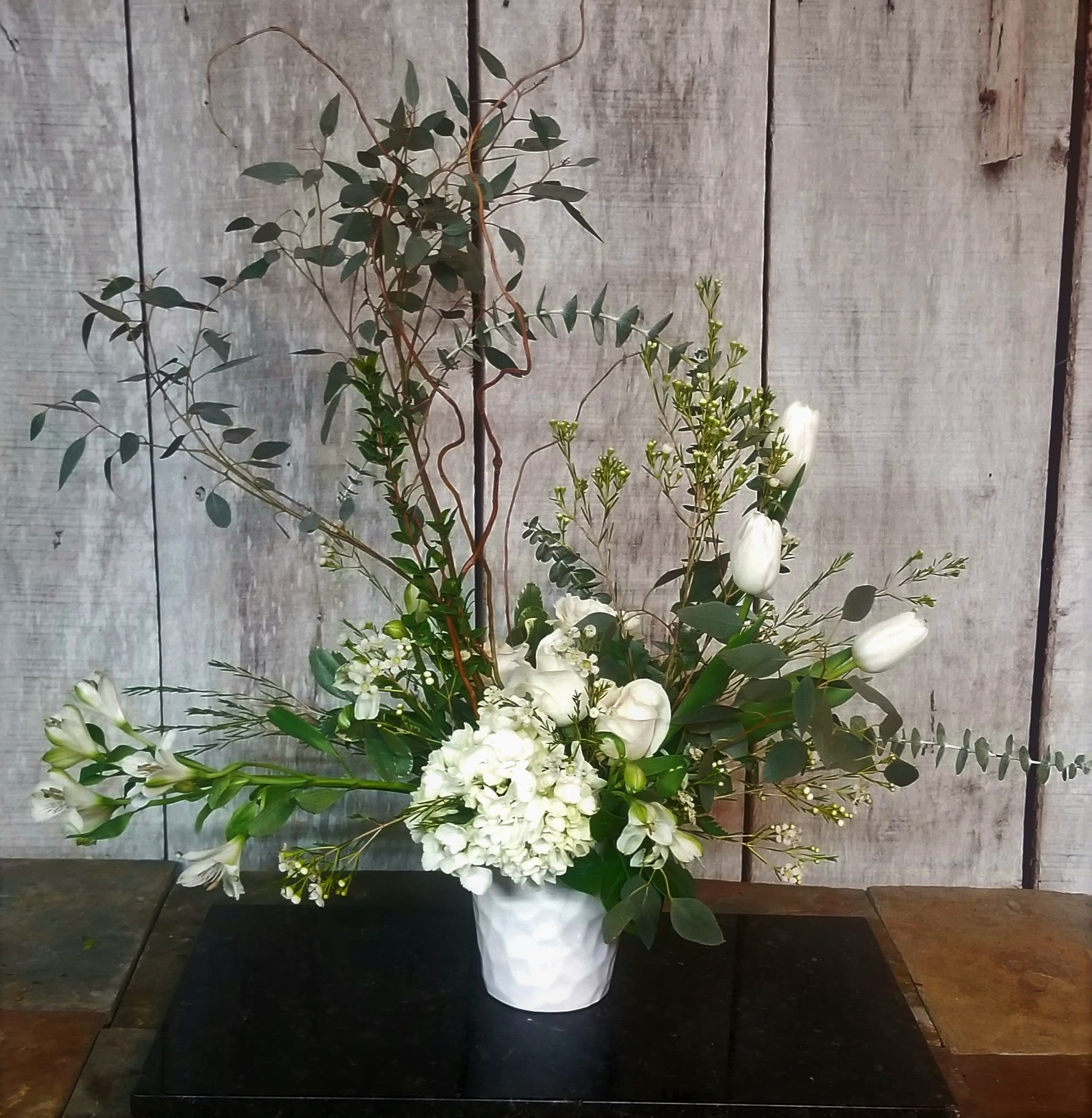 Tall white floral arrangement in a white vase with airy greenery