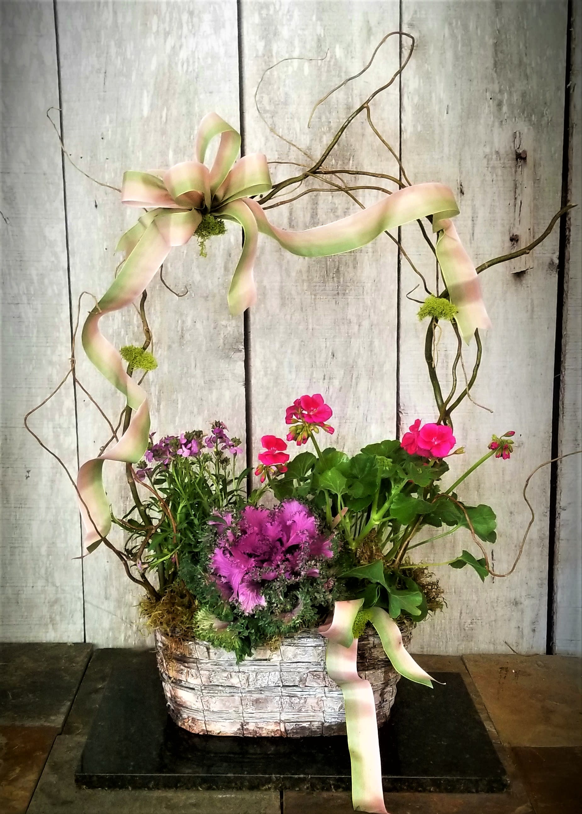 Basket arrangement with pink flowers and ribbon on a twig frame