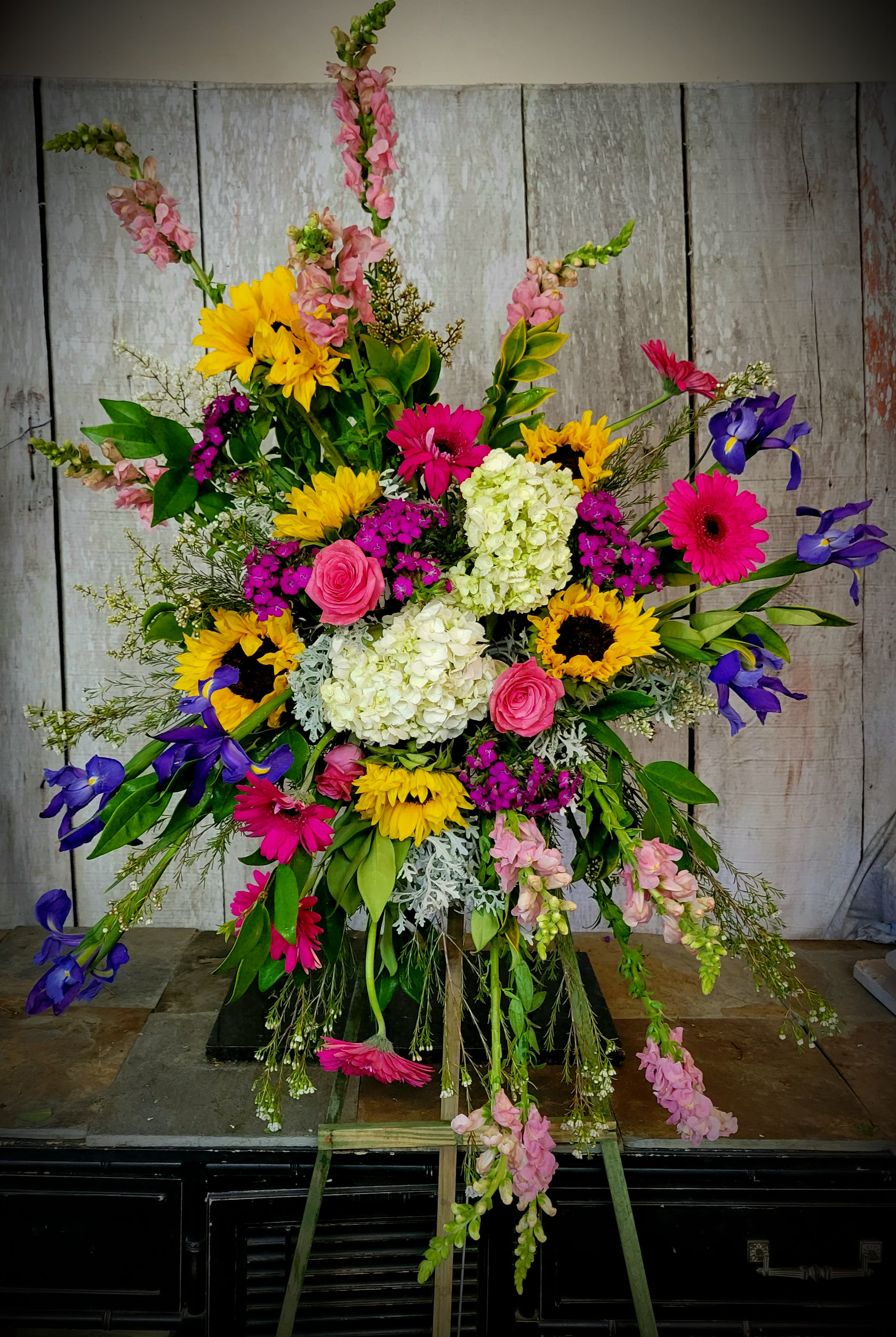 Large colorful standing floral spray with sunflowers, gerberas, roses, and irises