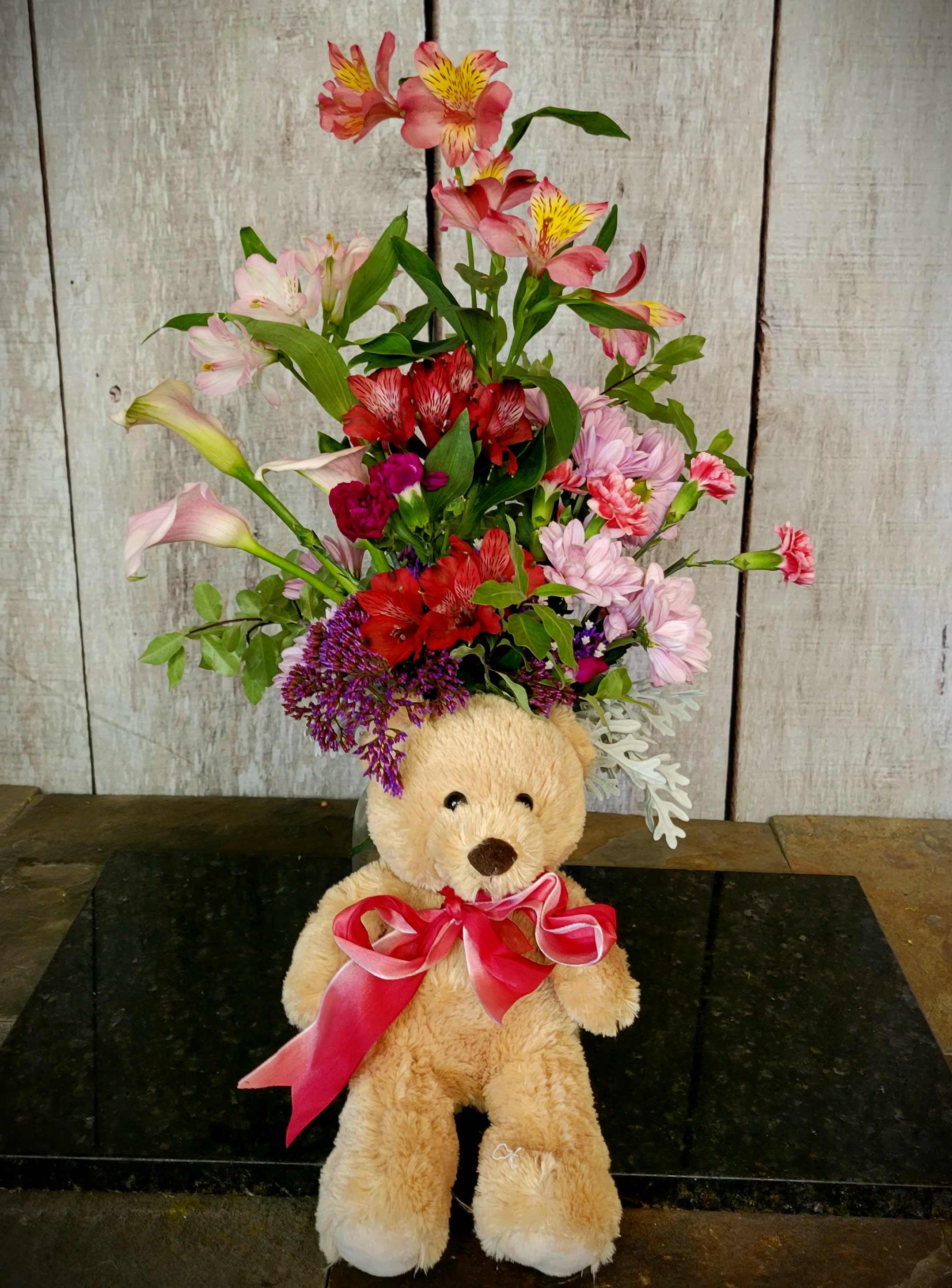 Teddy bear with a mixed flower arrangement and pink ribbon
