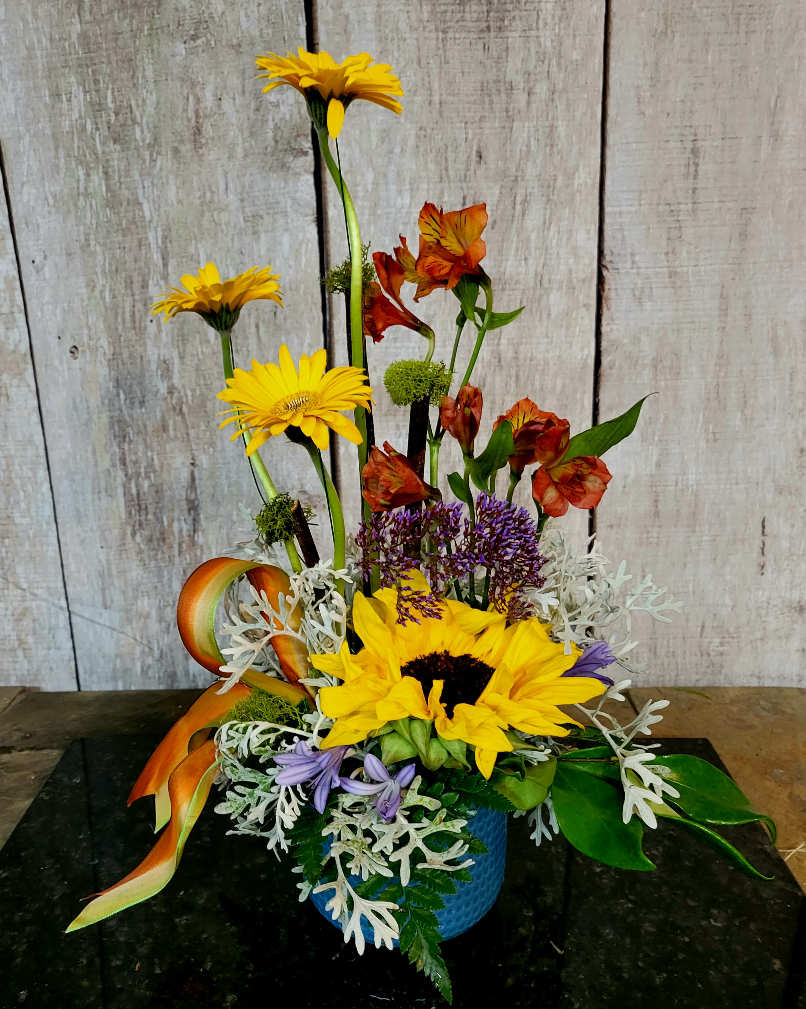 Mixed floral arrangement with yellow gerberas and sunflowers in a blue vase