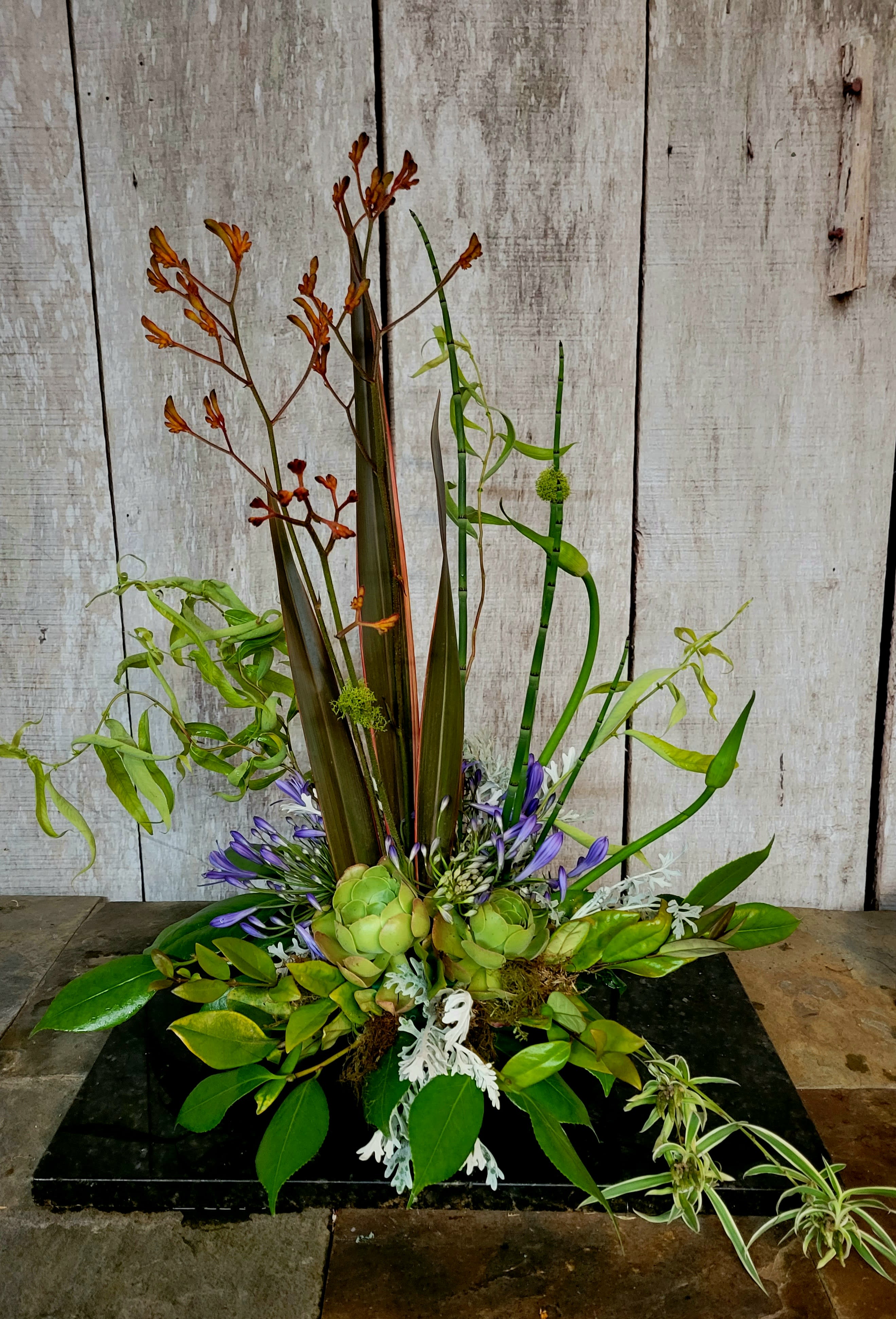 Tall tropical arrangement with green succulents and purple flowers on a black base