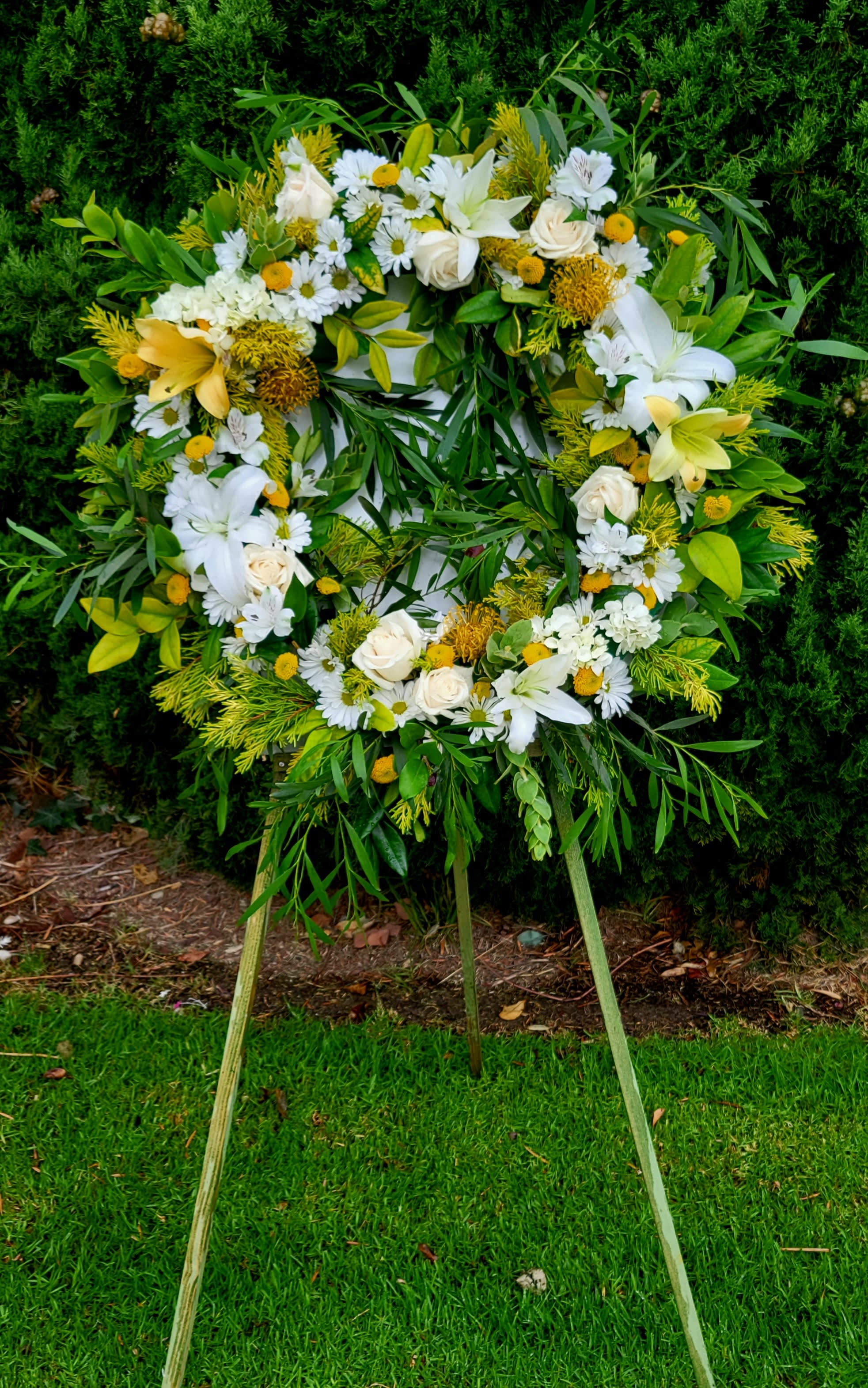 Circular standing wreath of white and yellow flowers on an easel