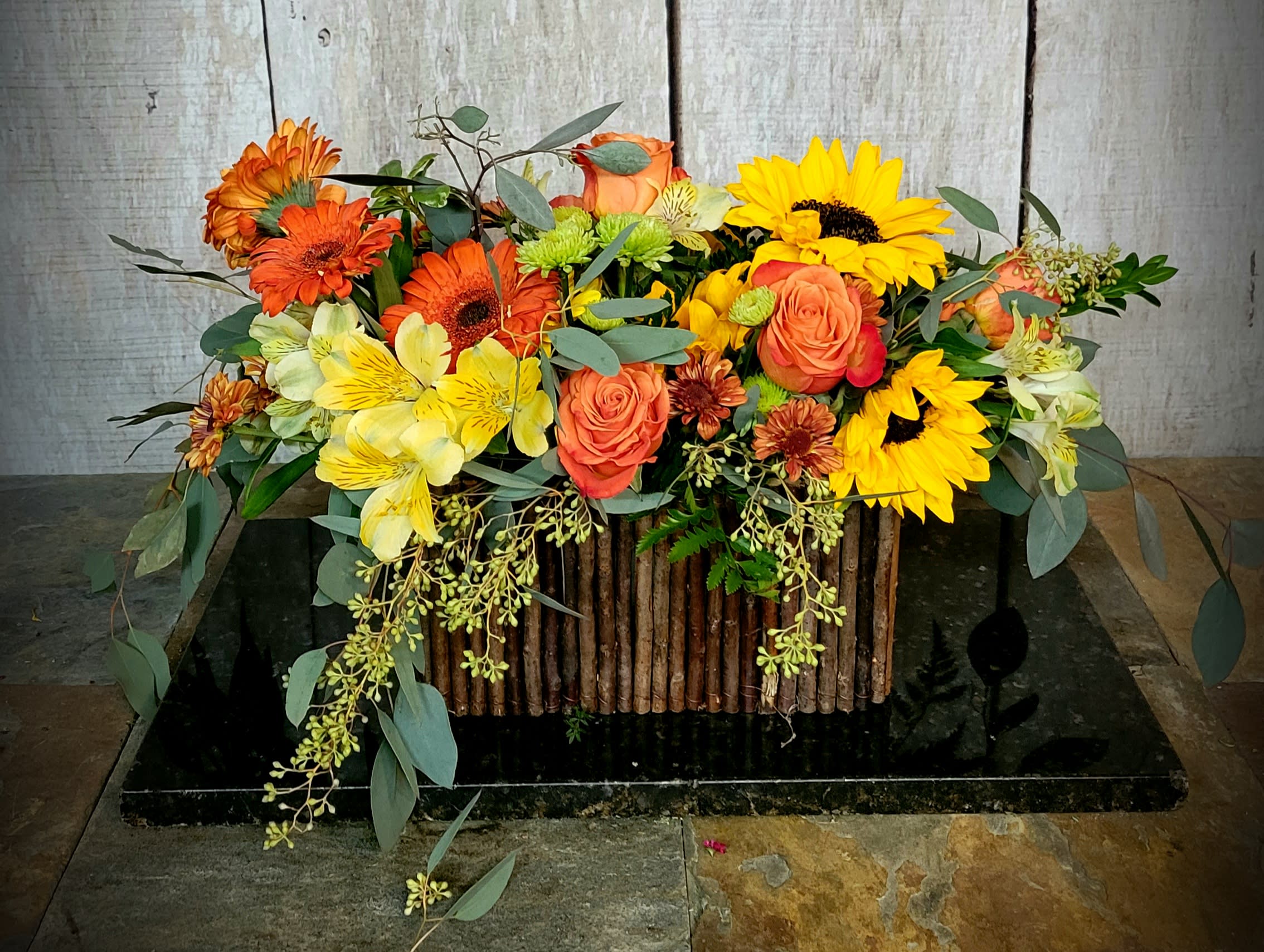 Mixed bouquet of sunflowers, orange roses, and yellow flowers in a rustic container