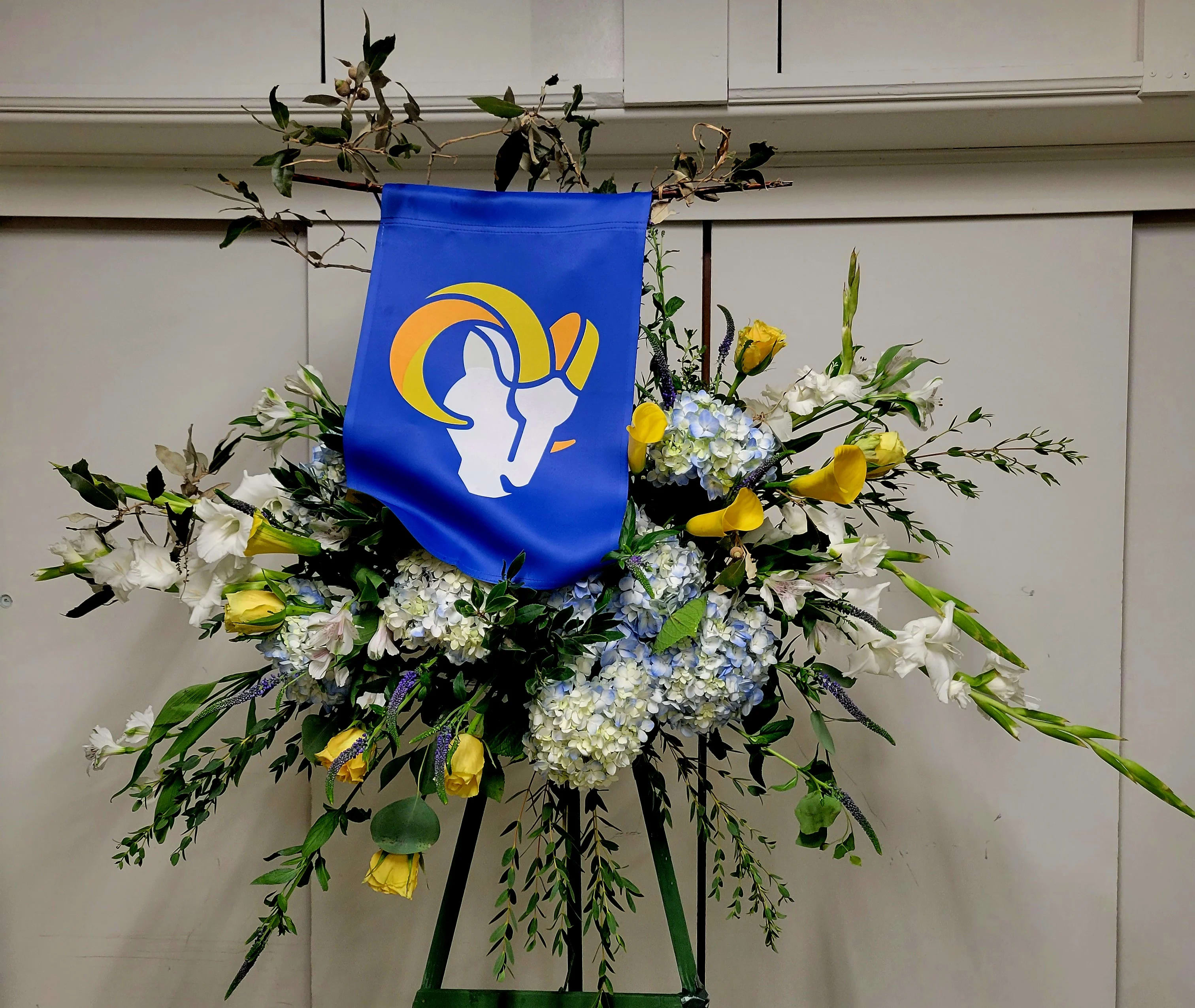 Large floral standing spray with blue banner and yellow-white flowers