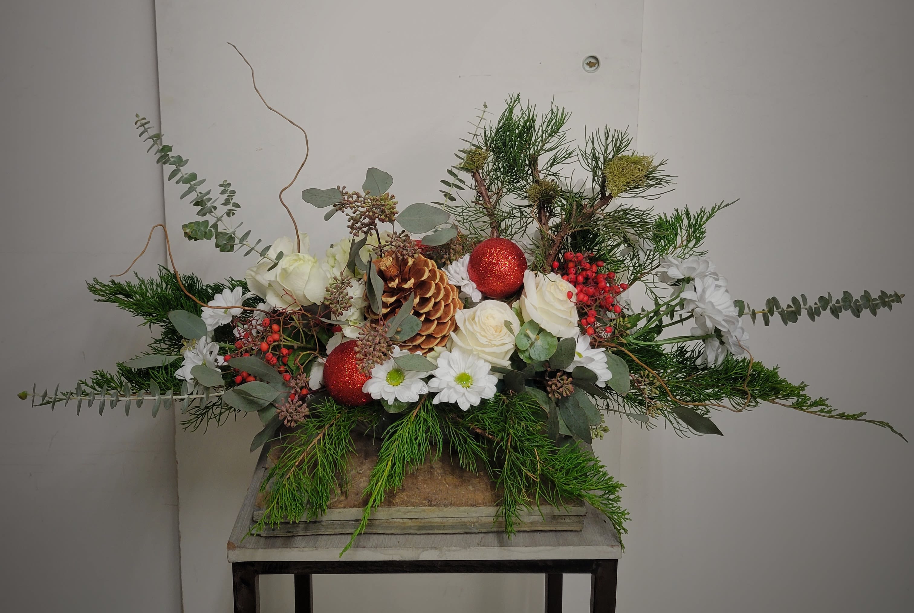 Holiday floral arrangement with white roses, daisies, pinecones, and red ornaments