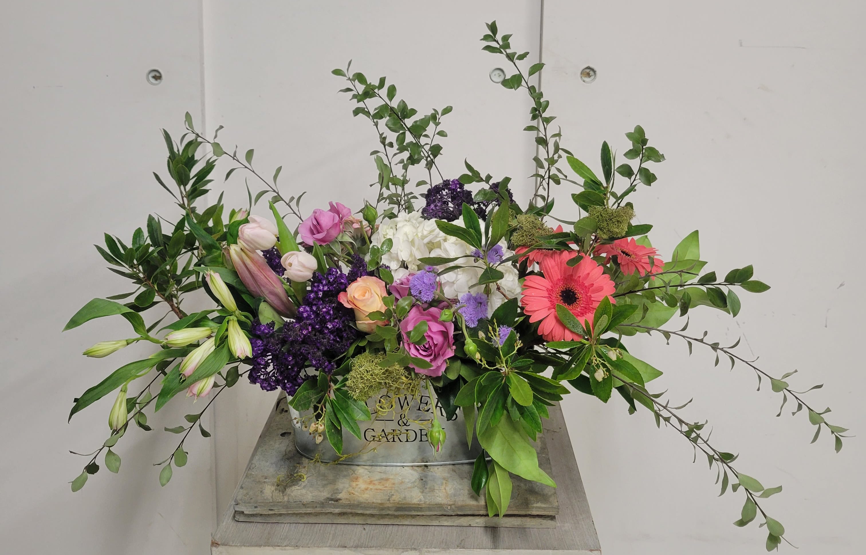 Mixed floral arrangement with roses, lilies, and gerbera daisies in a metal container
