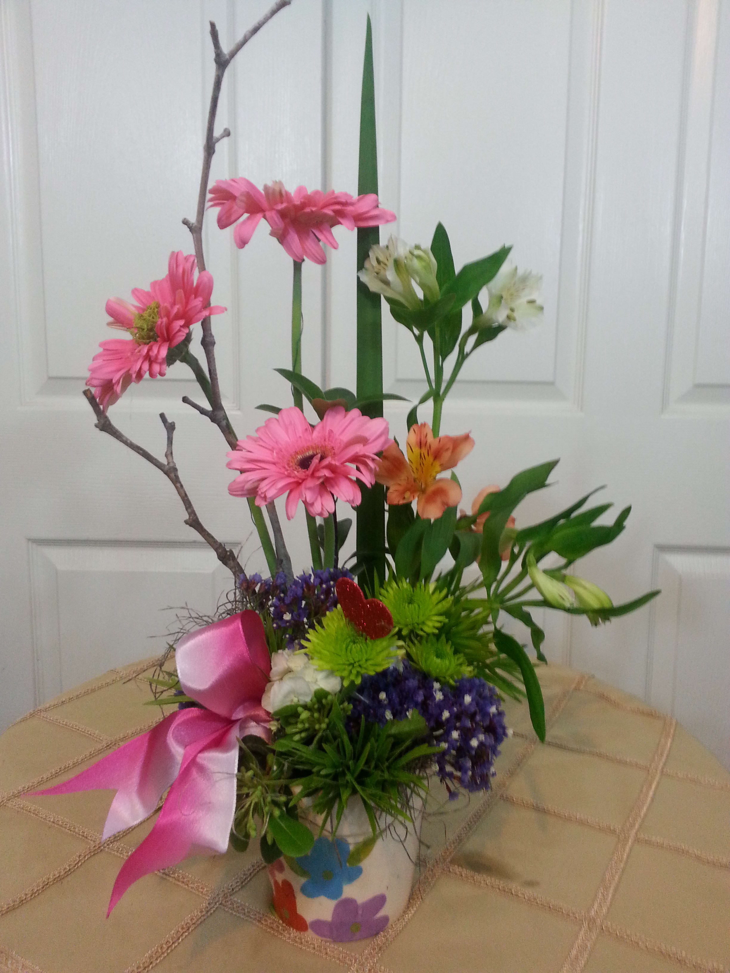 Pink and orange mixed flower arrangement in a decorated vase with a pink ribbon