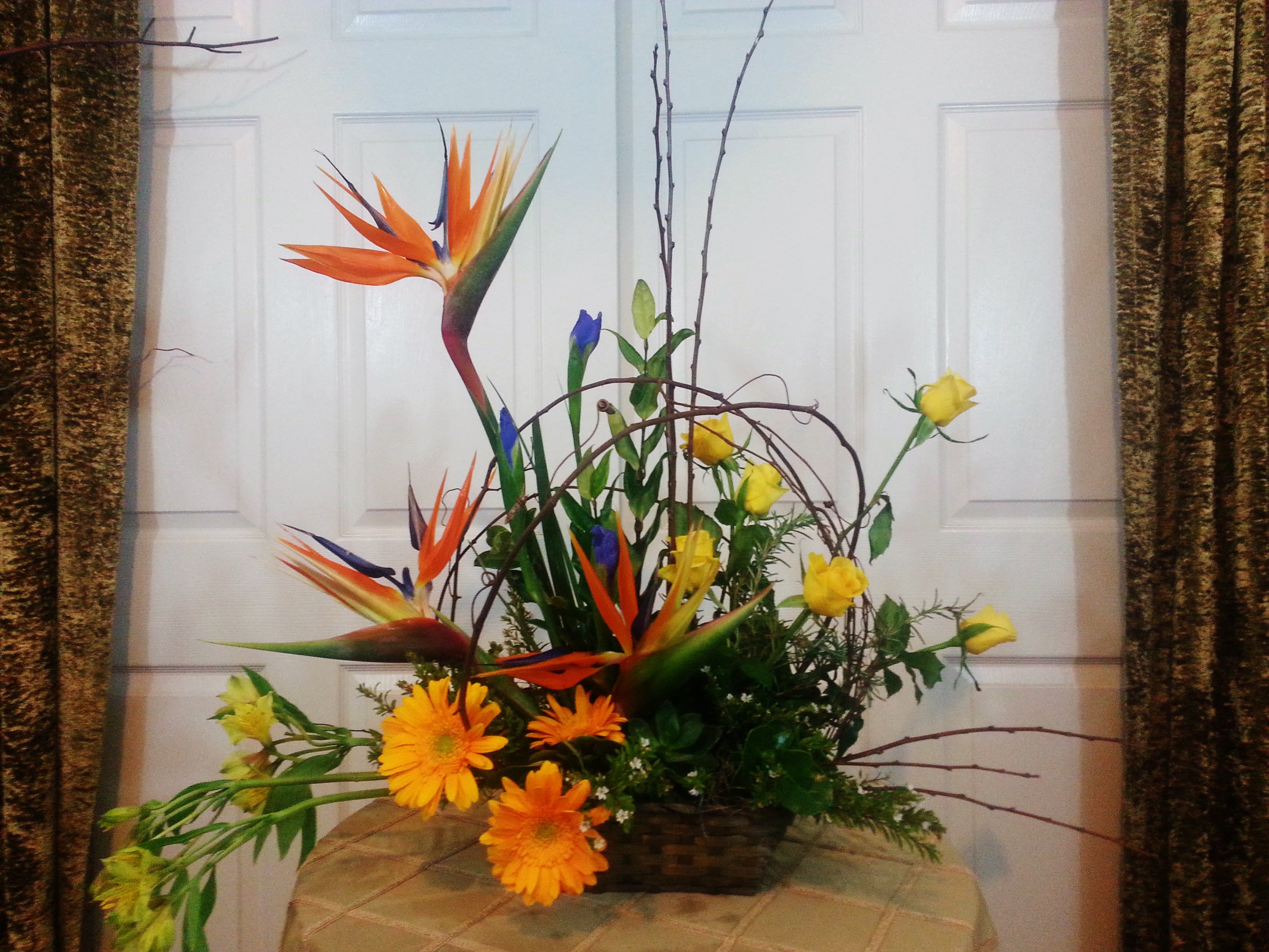 Tropical floral arrangement with orange bird-of-paradise and yellow roses in a basket