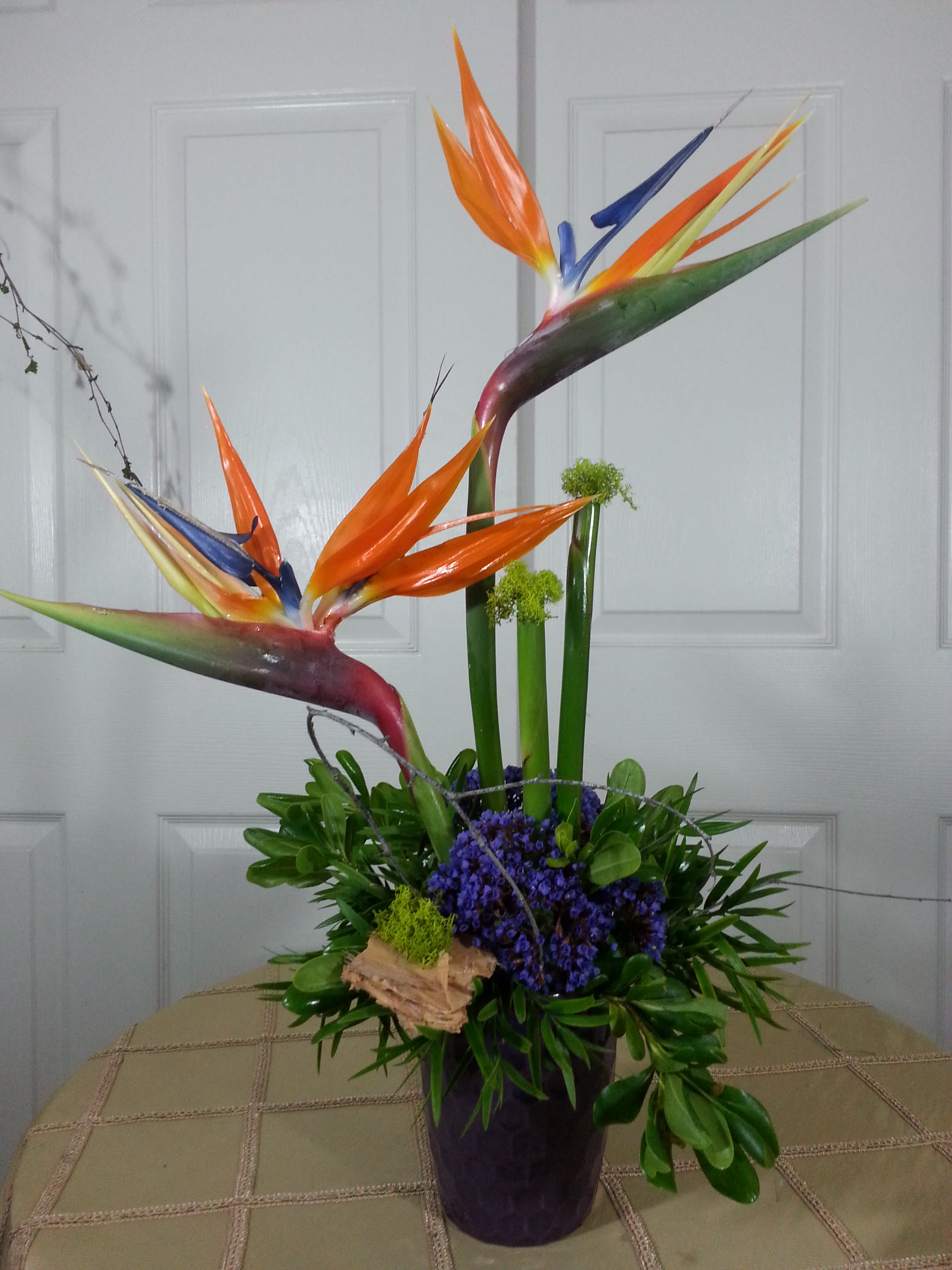 Tropical bird-of-paradise arrangement in a dark vase with purple flowers