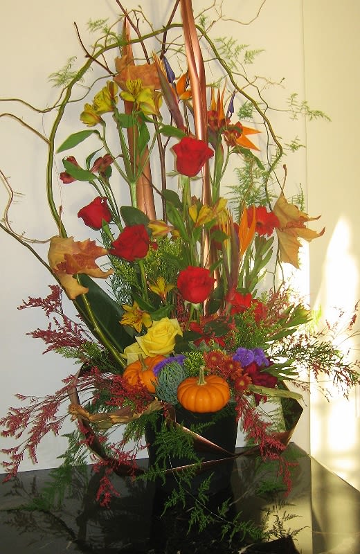 Tall autumn floral arrangement with roses and small pumpkins in a black container