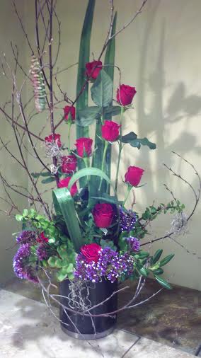 Tall arrangement of pink roses and purple flowers in a black container