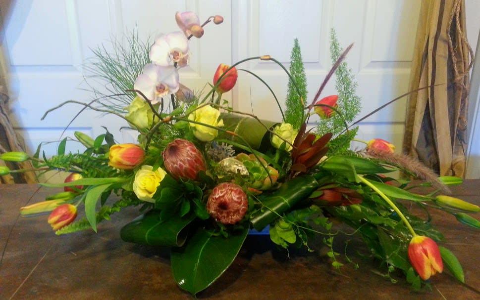Low floral arrangement with orchids, tulips, and protea in a container