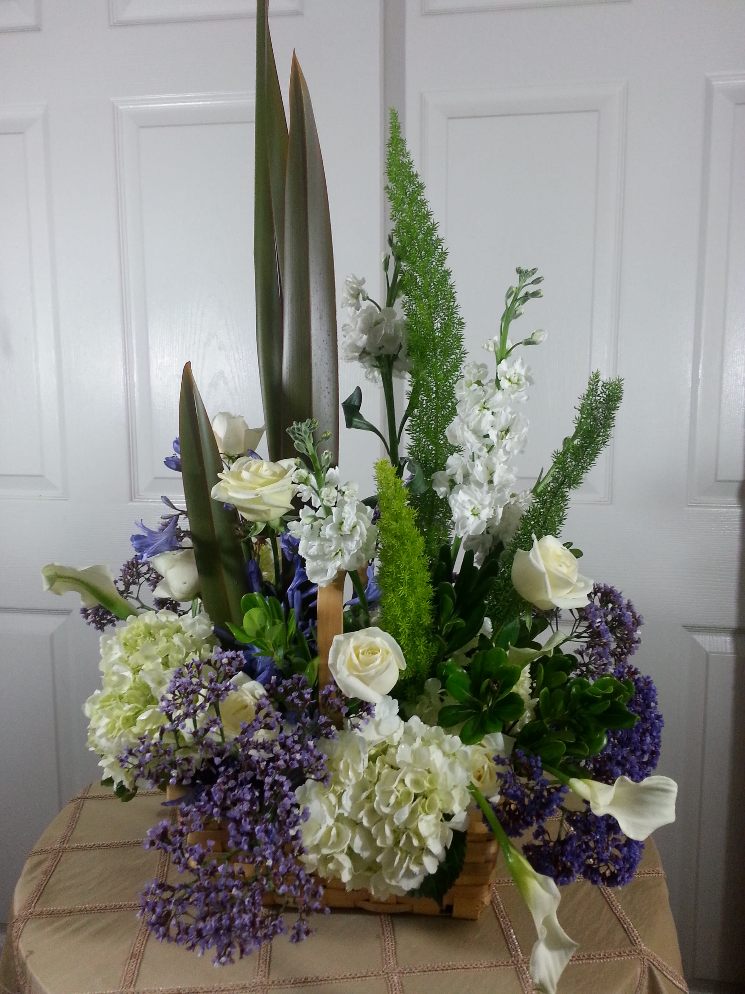 Tall floral arrangement with white roses, calla lilies, and purple filler flowers