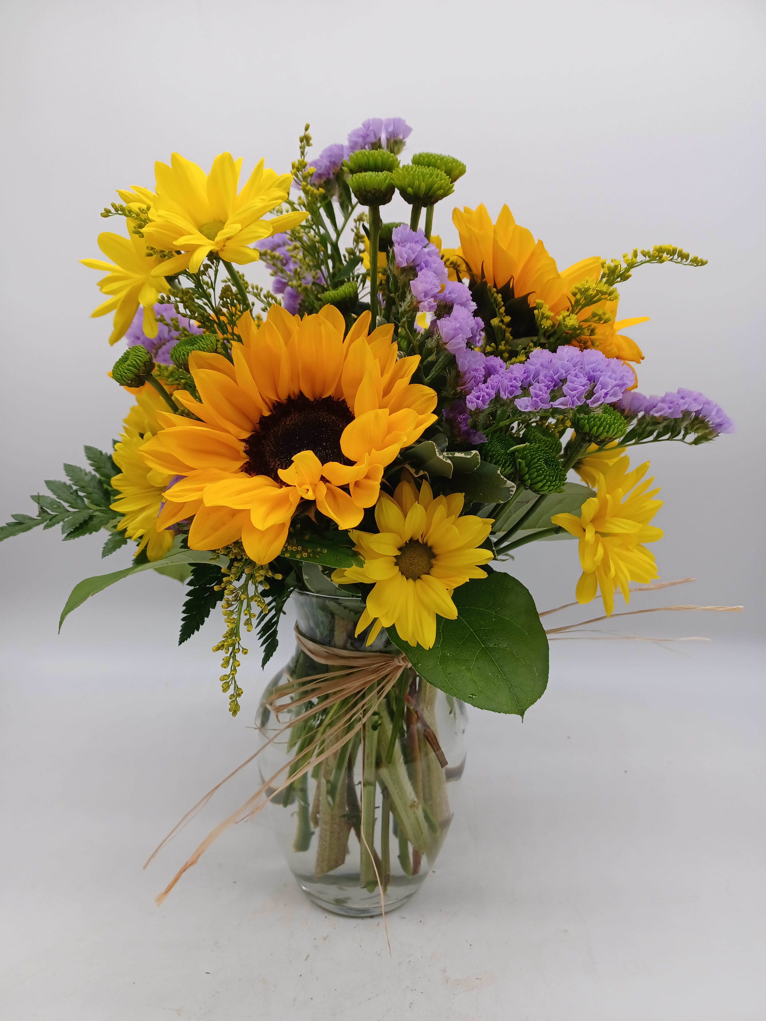 Bouquet of yellow sunflowers and purple flowers in a glass vase