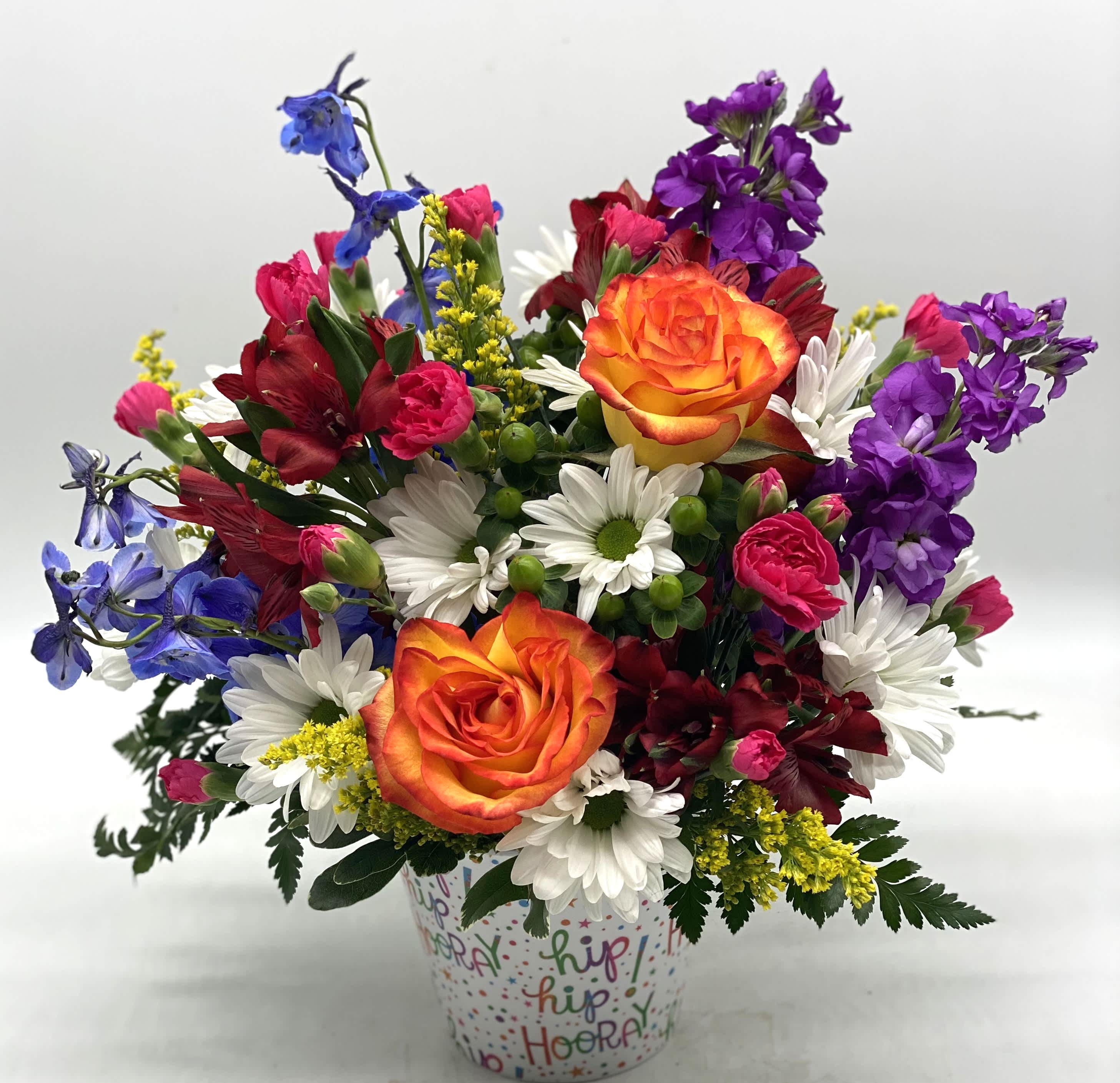 Colorful mixed bouquet in a patterned cup with orange roses and daisies