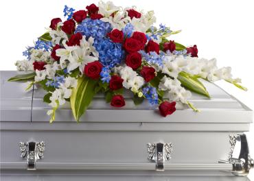 Red roses, white lilies, and blue flowers arranged on a white casket