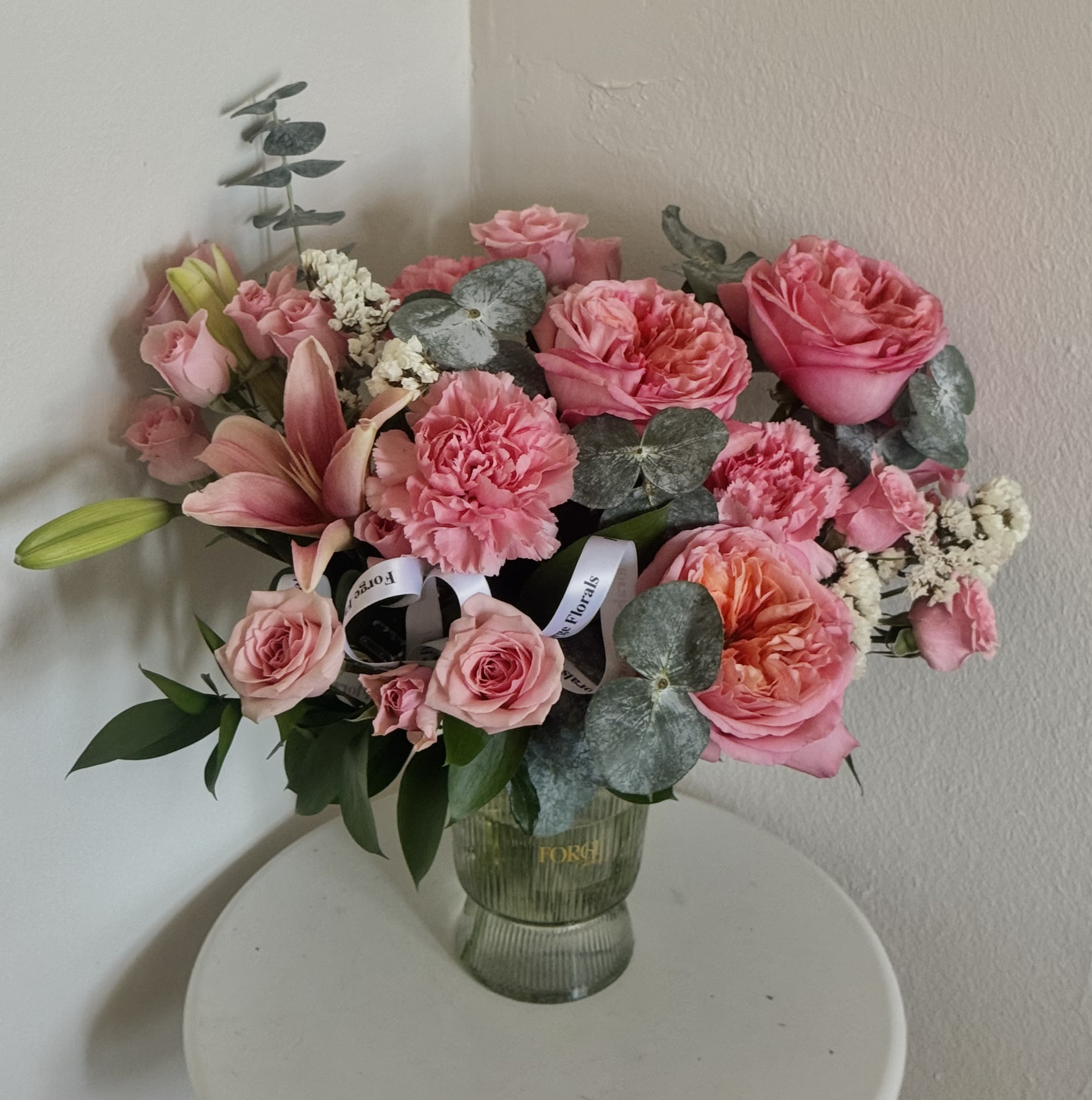 Romance vase- garden rose, lily, mini roses, eucalyptus  - A lush garden-style arrangement featuring soft pink roses, spray roses, carnations and a fresh lily, accented with eucalyptus and seasonal greenery. Designed in a plastic vase, this romantic bouquet brings warmth and elegance to any space.  Perfect for birthdays, anniversaries, or simply brightening someone’s day.