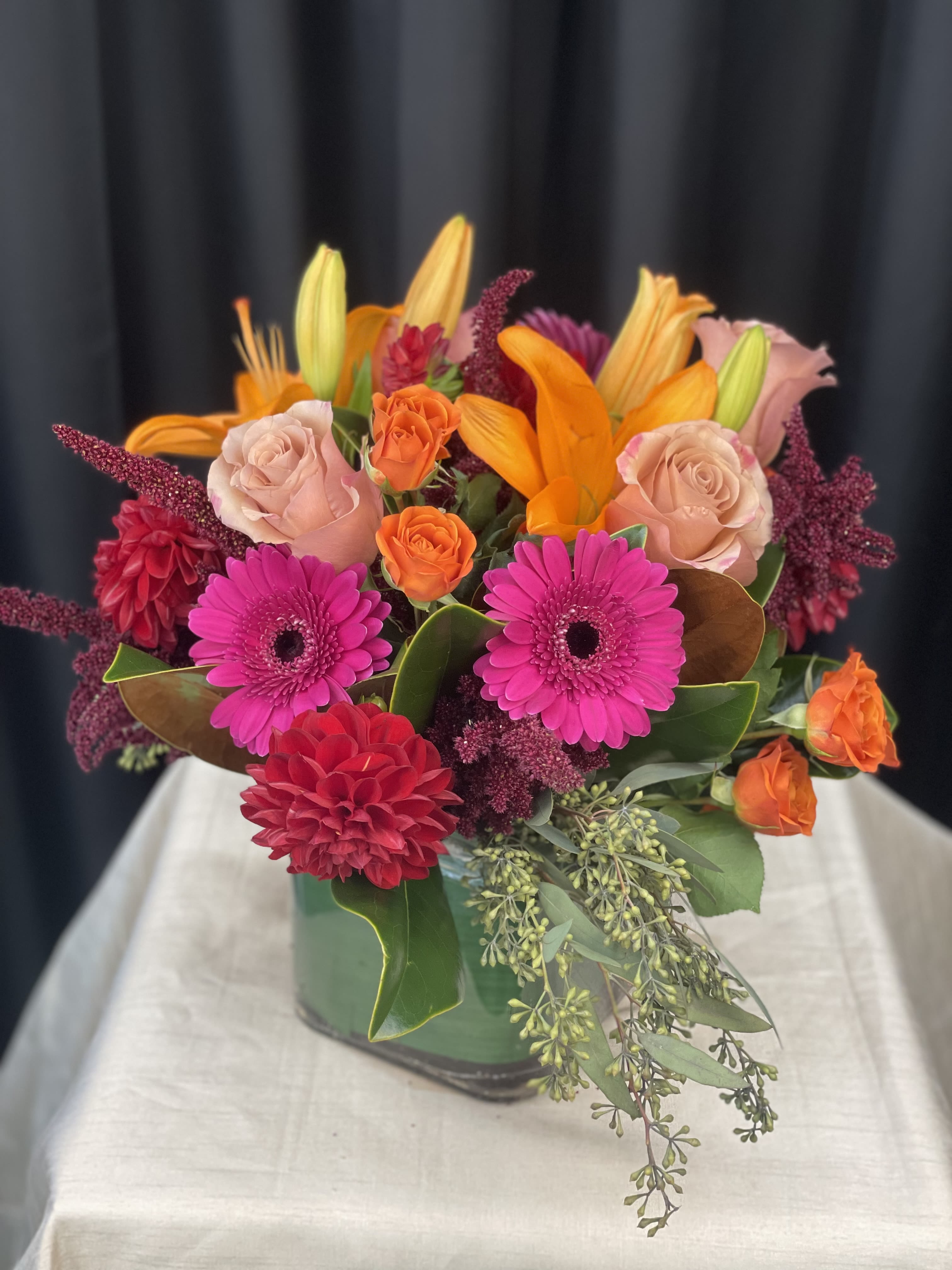 Bright mixed bouquet in a green vase with pink, orange, and red blooms