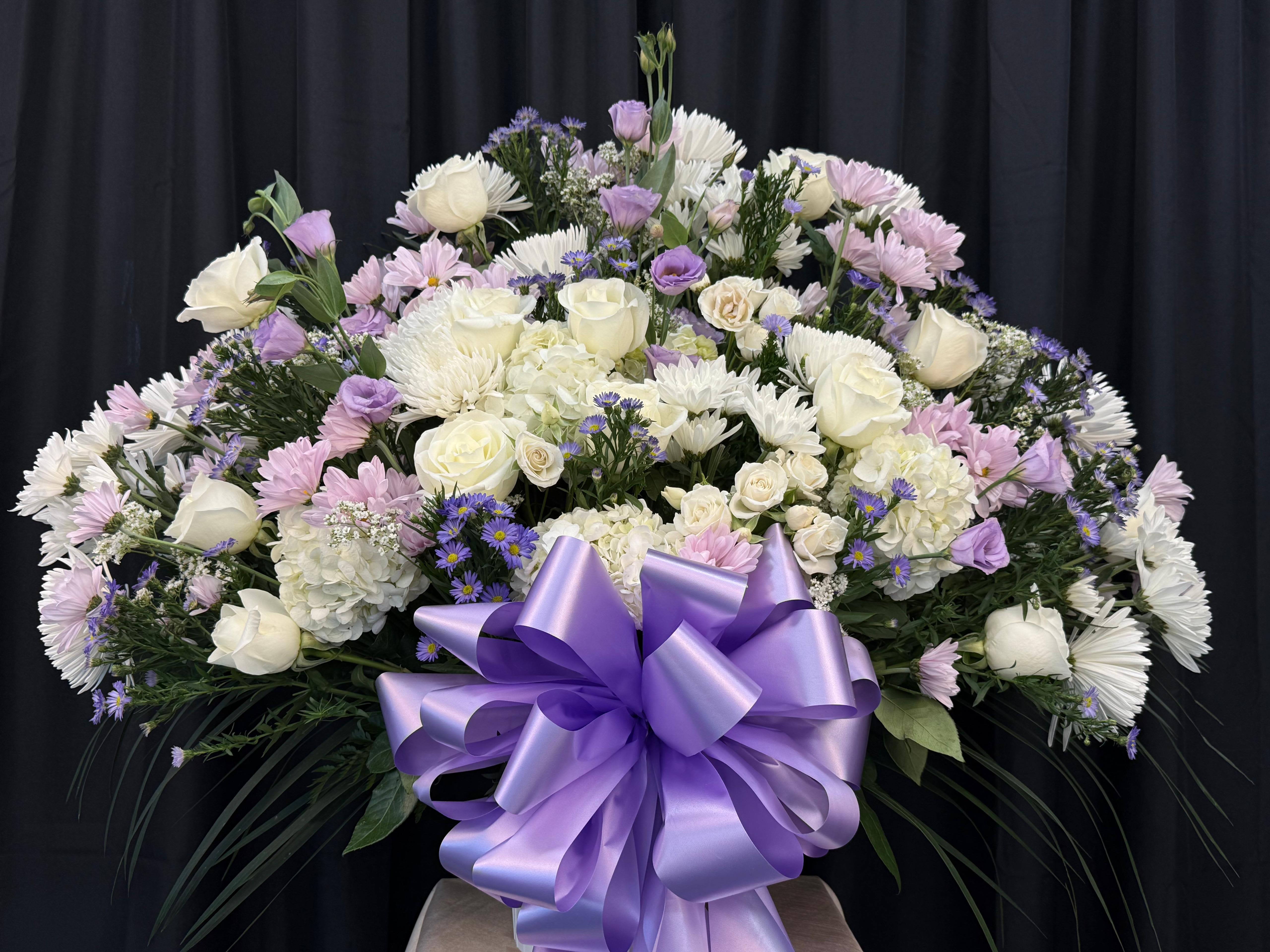 Large lavender and white floral arrangement with a purple ribbon bow