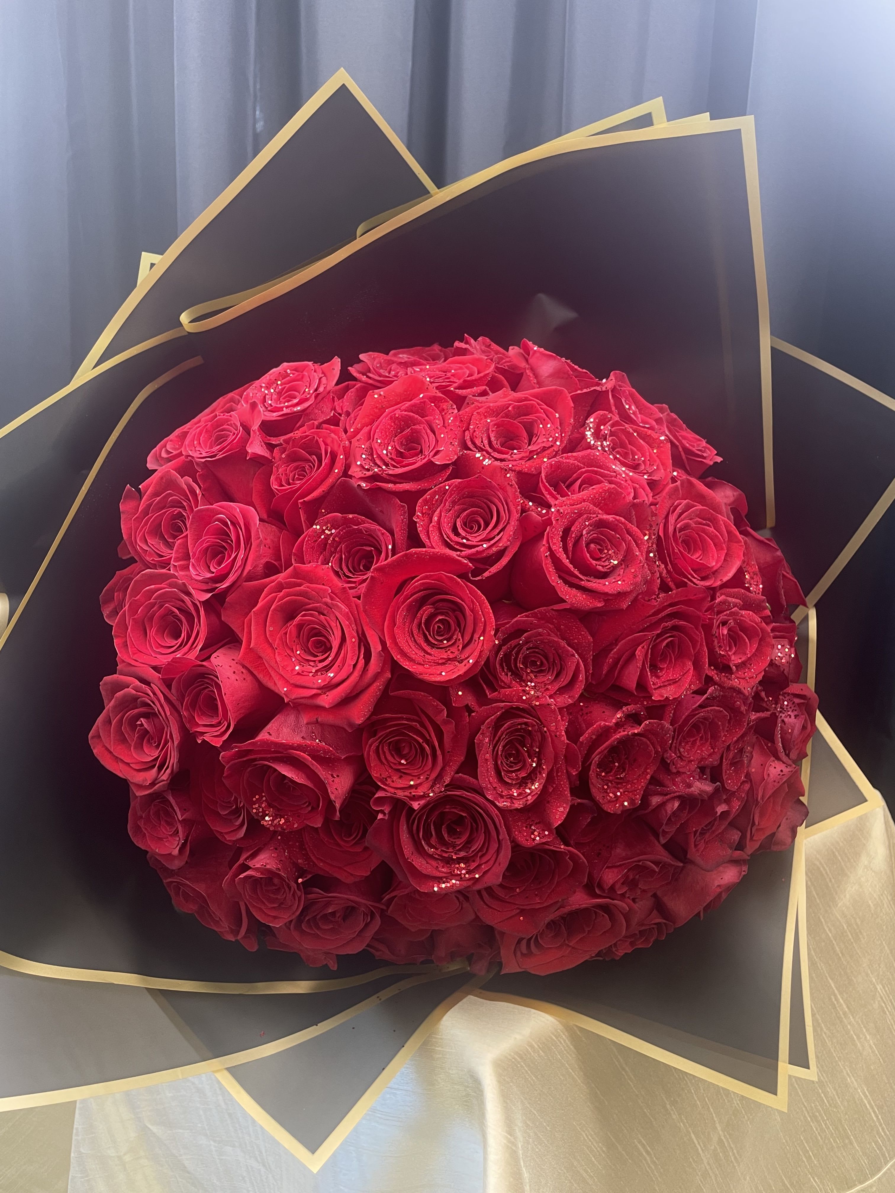 Round bouquet of red roses wrapped in black and gold paper