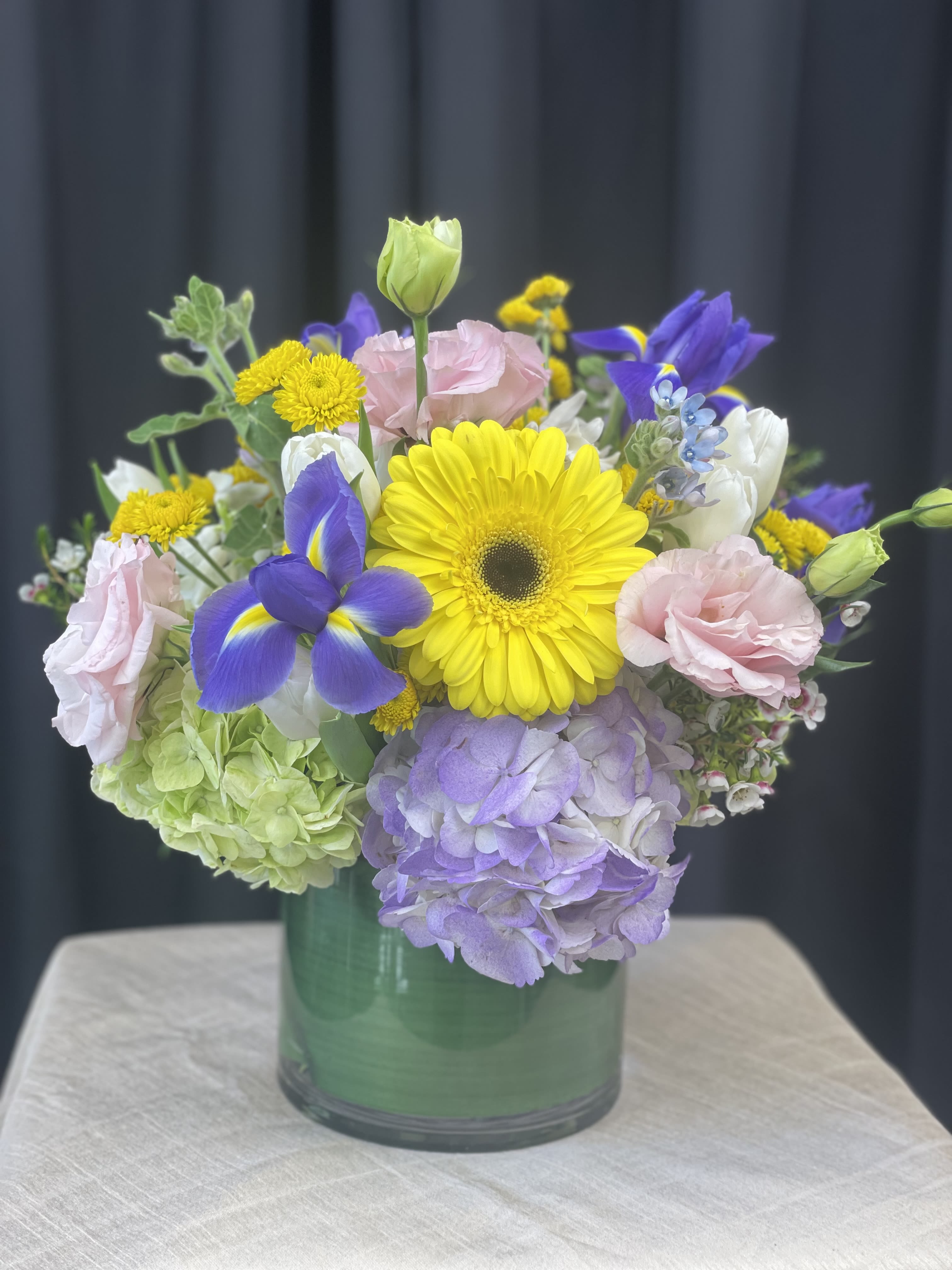 Mixed bouquet in a green glass vase with yellow, purple, pink, and white blooms
