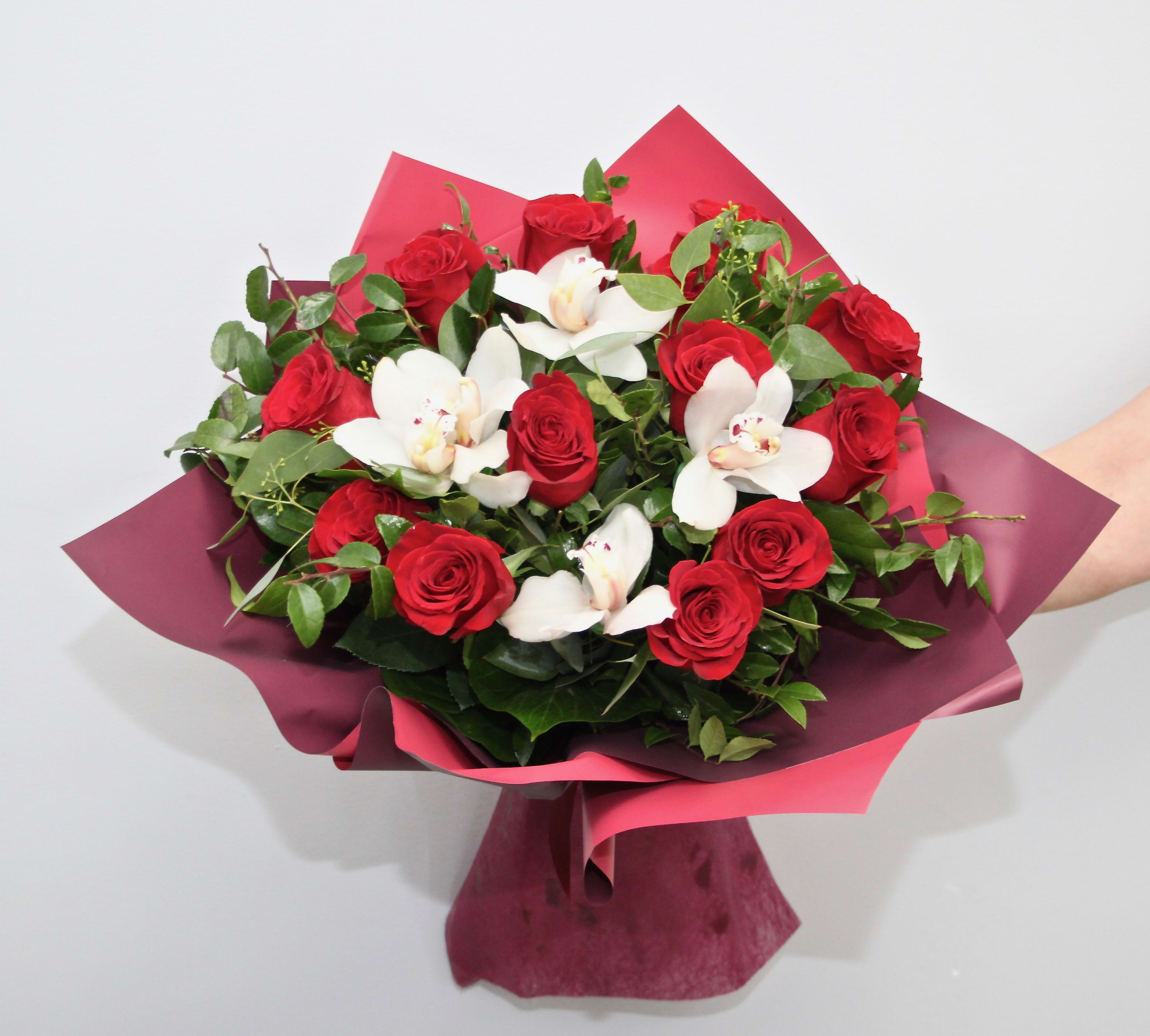 Hand-tied bouquet of red roses and white orchids wrapped in burgundy and pink paper