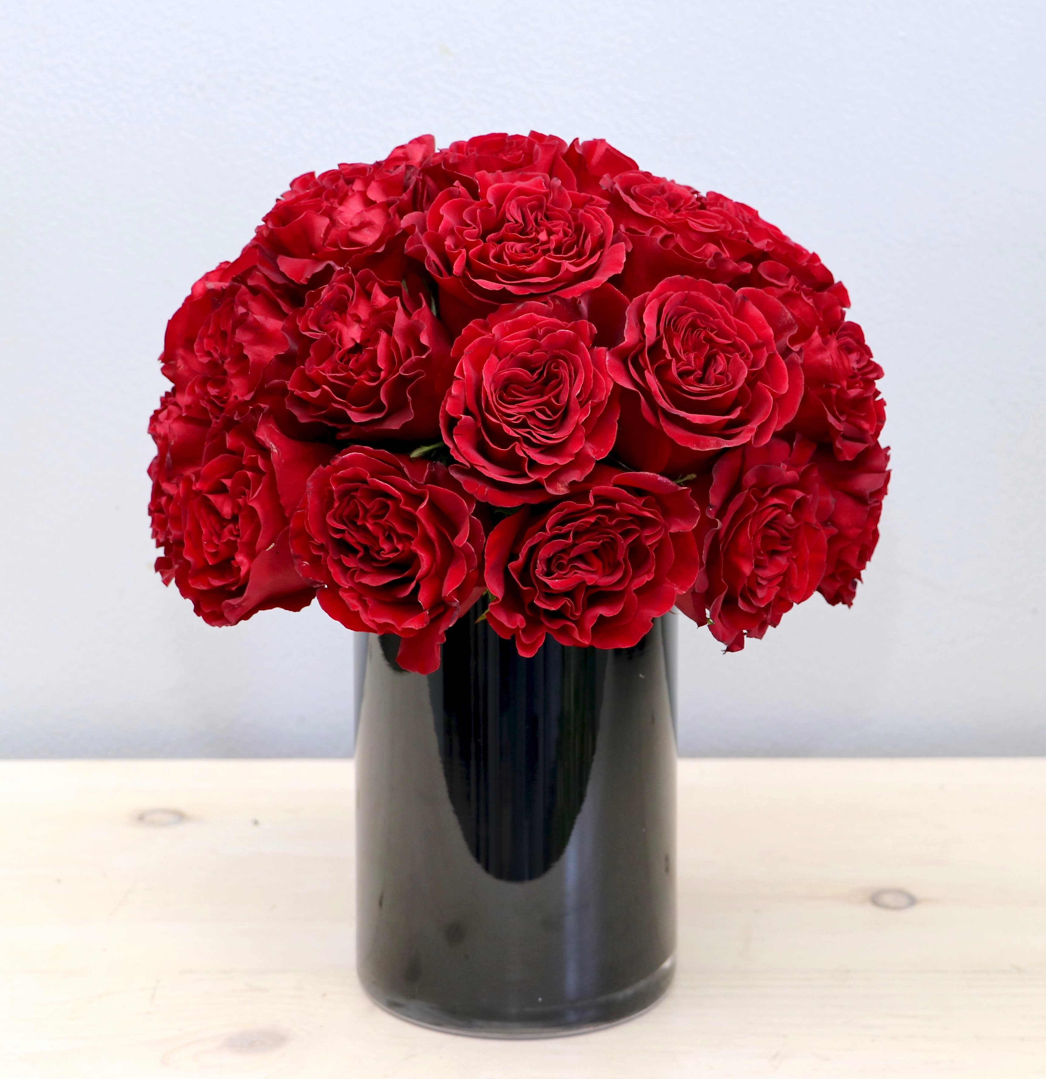 Compact arrangement of red roses in a glossy black cylinder vase