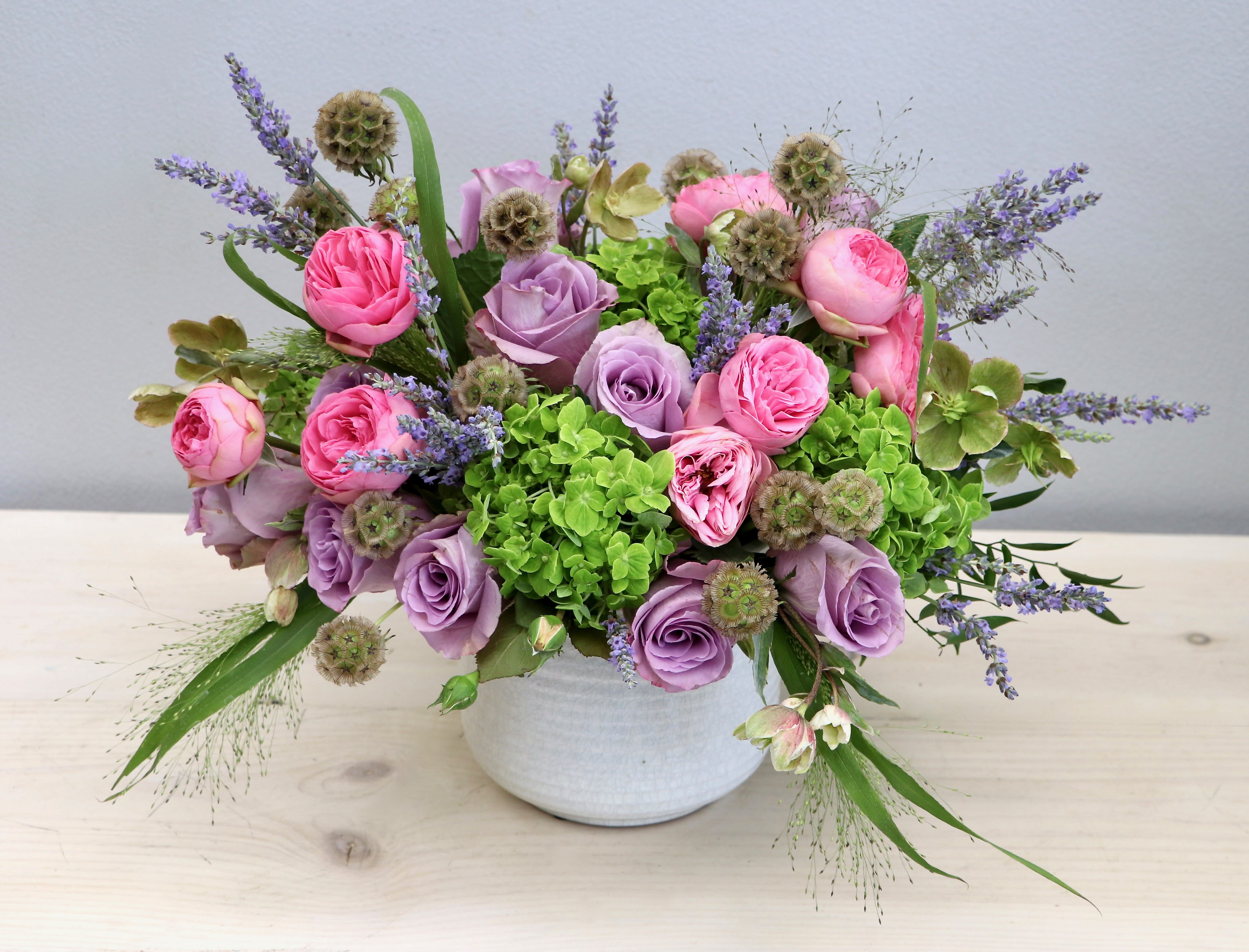 Low arrangement of pink and lavender roses with green hydrangeas in a white bowl vase