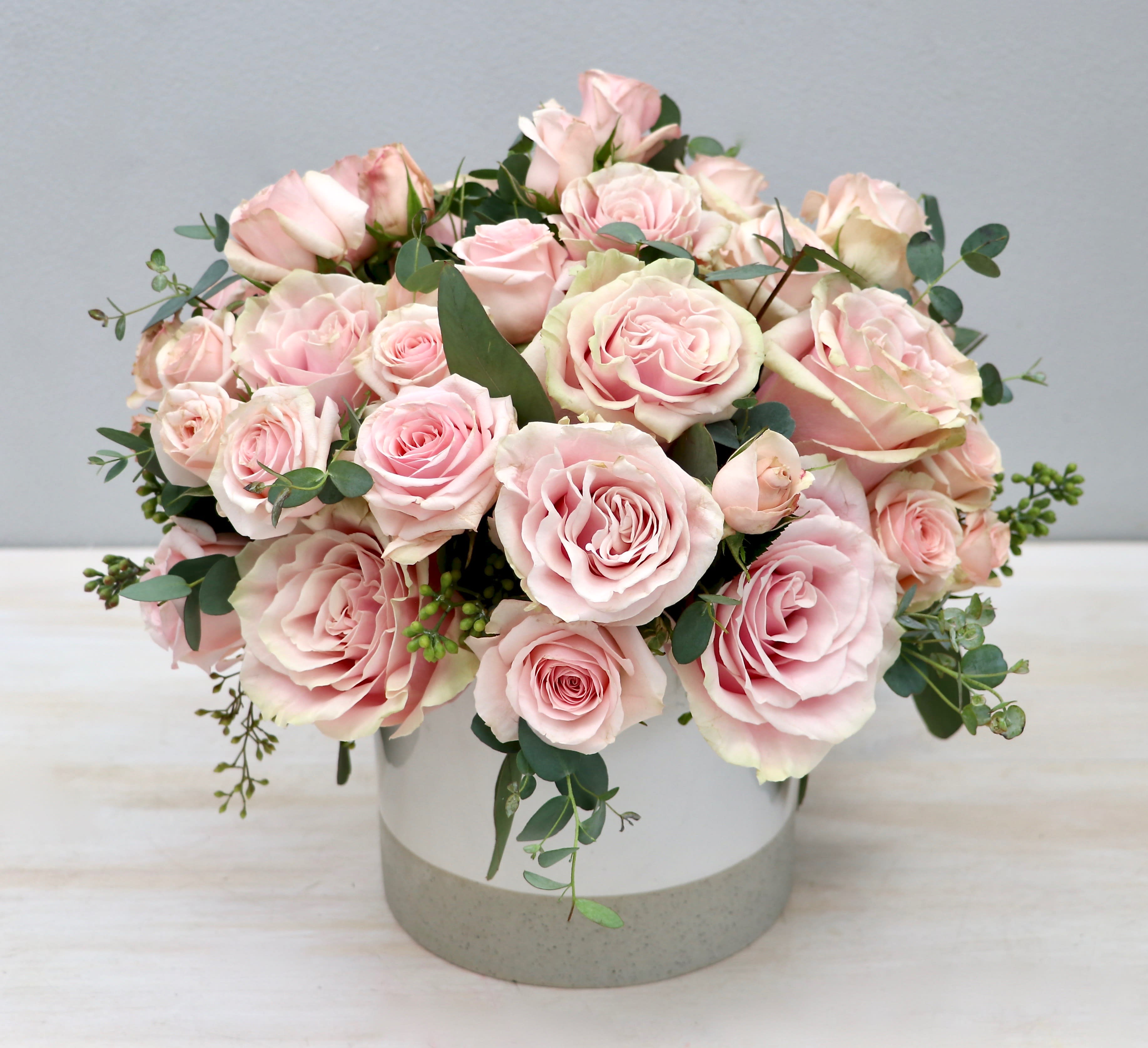 Low round arrangement of pale pink roses in a white and gray ceramic cylinder vase