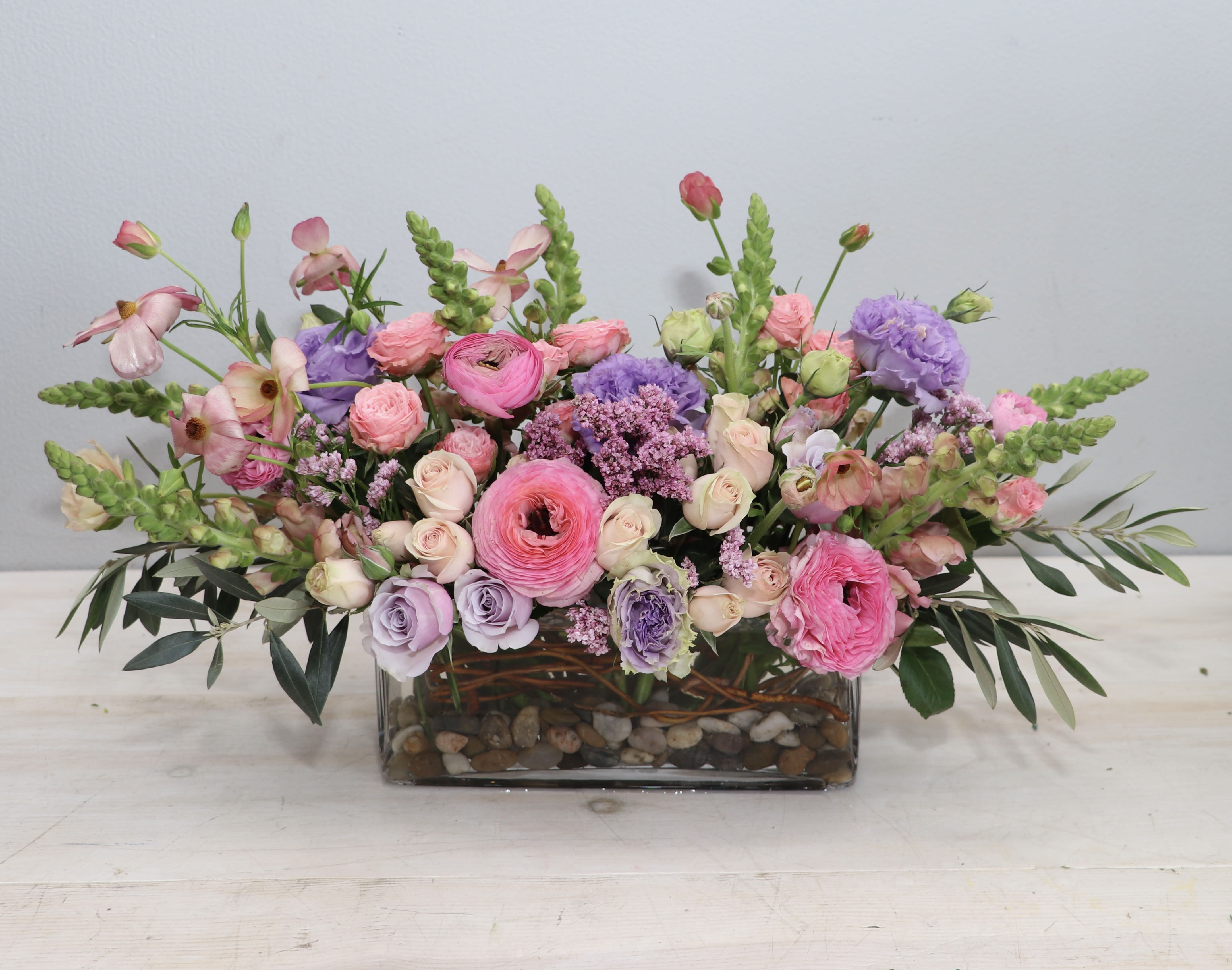 Low rectangular arrangement of pink and lavender flowers in a glass vase with river rocks