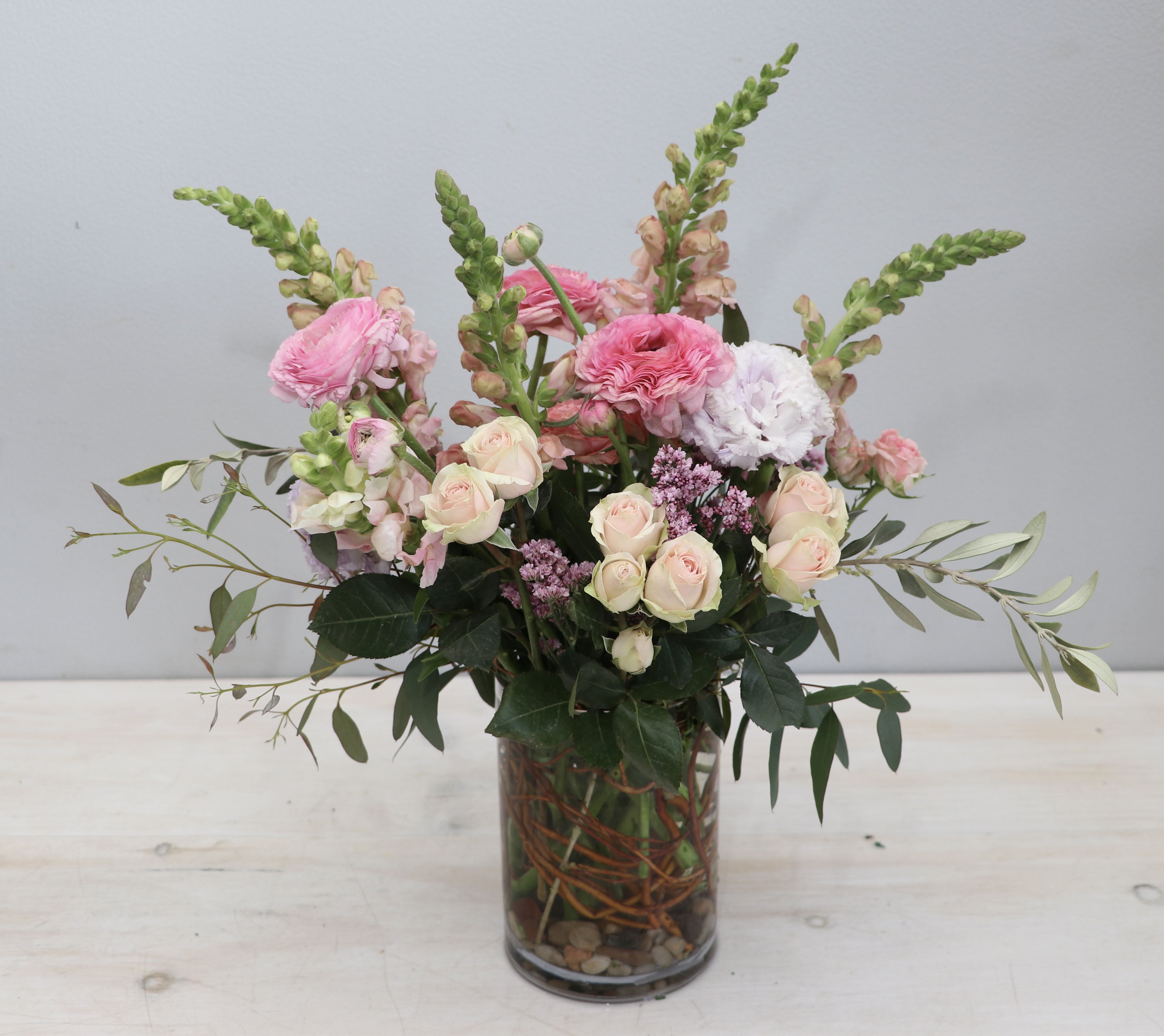 Tall pastel pink and white flower arrangement with roses and ranunculus in a clear glass vase.