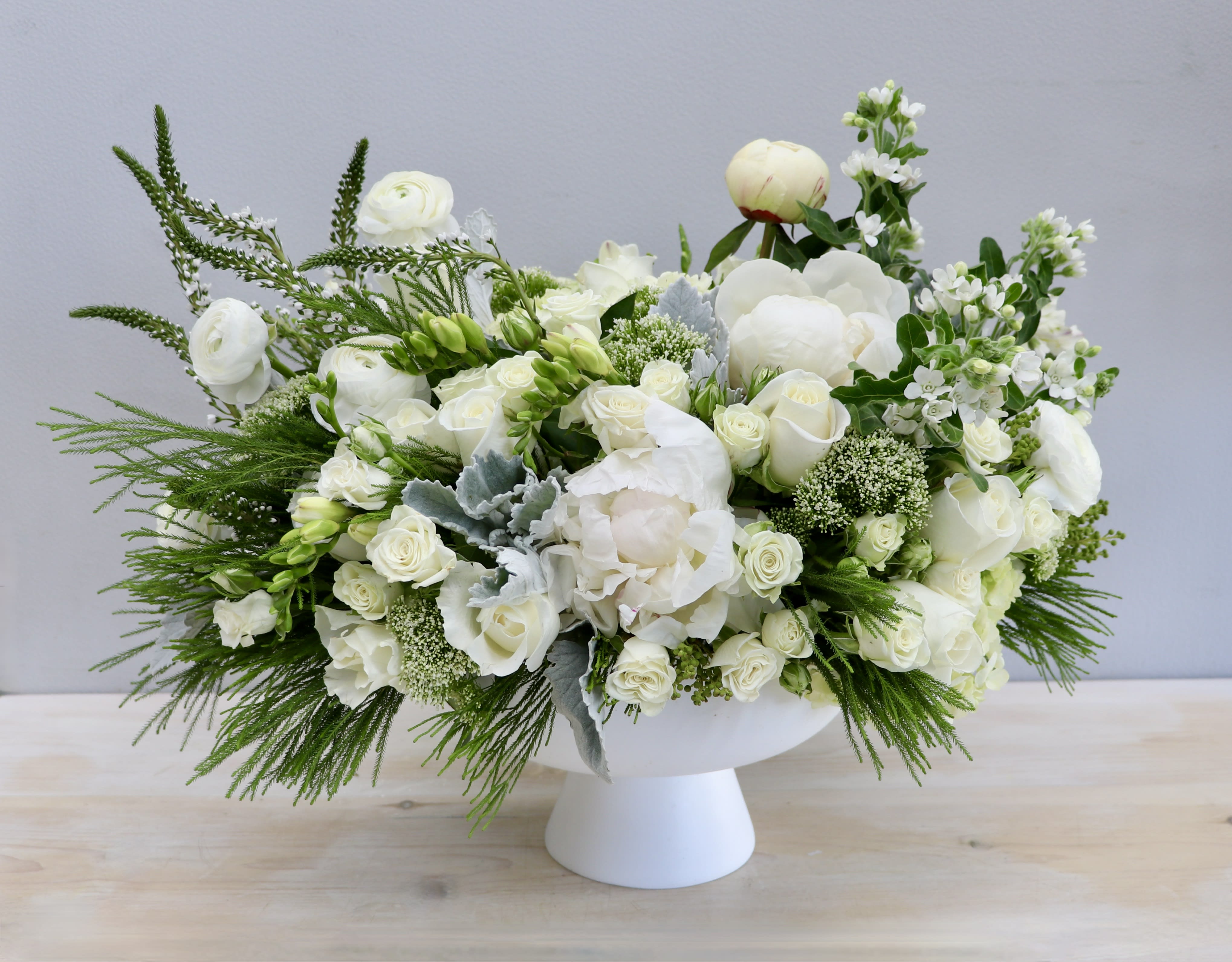 Low white pedestal arrangement with white roses, peonies, and other white blooms